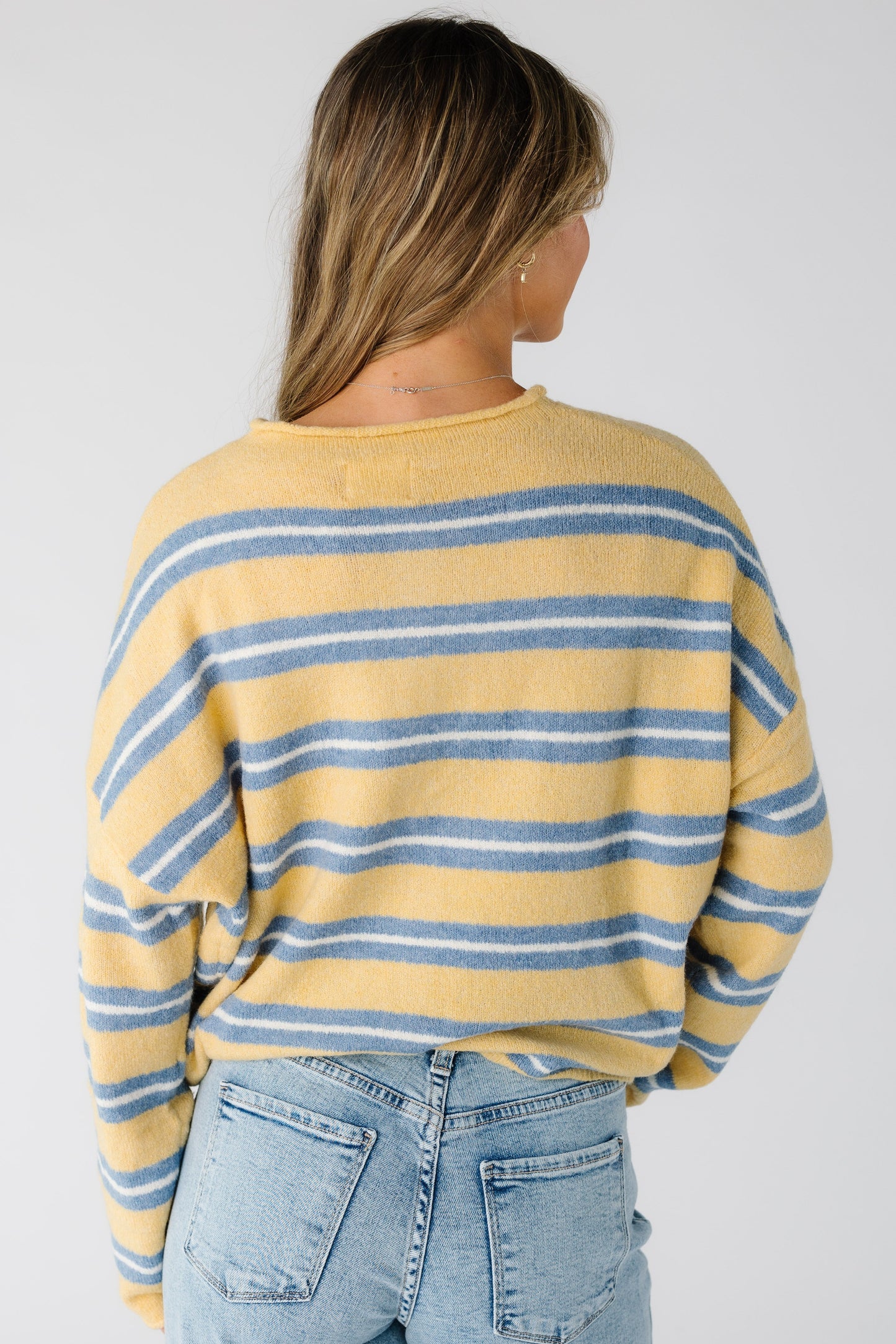 Back view of a woman wearing a yellow, blue and white stripe cardigan with long sleeves.
