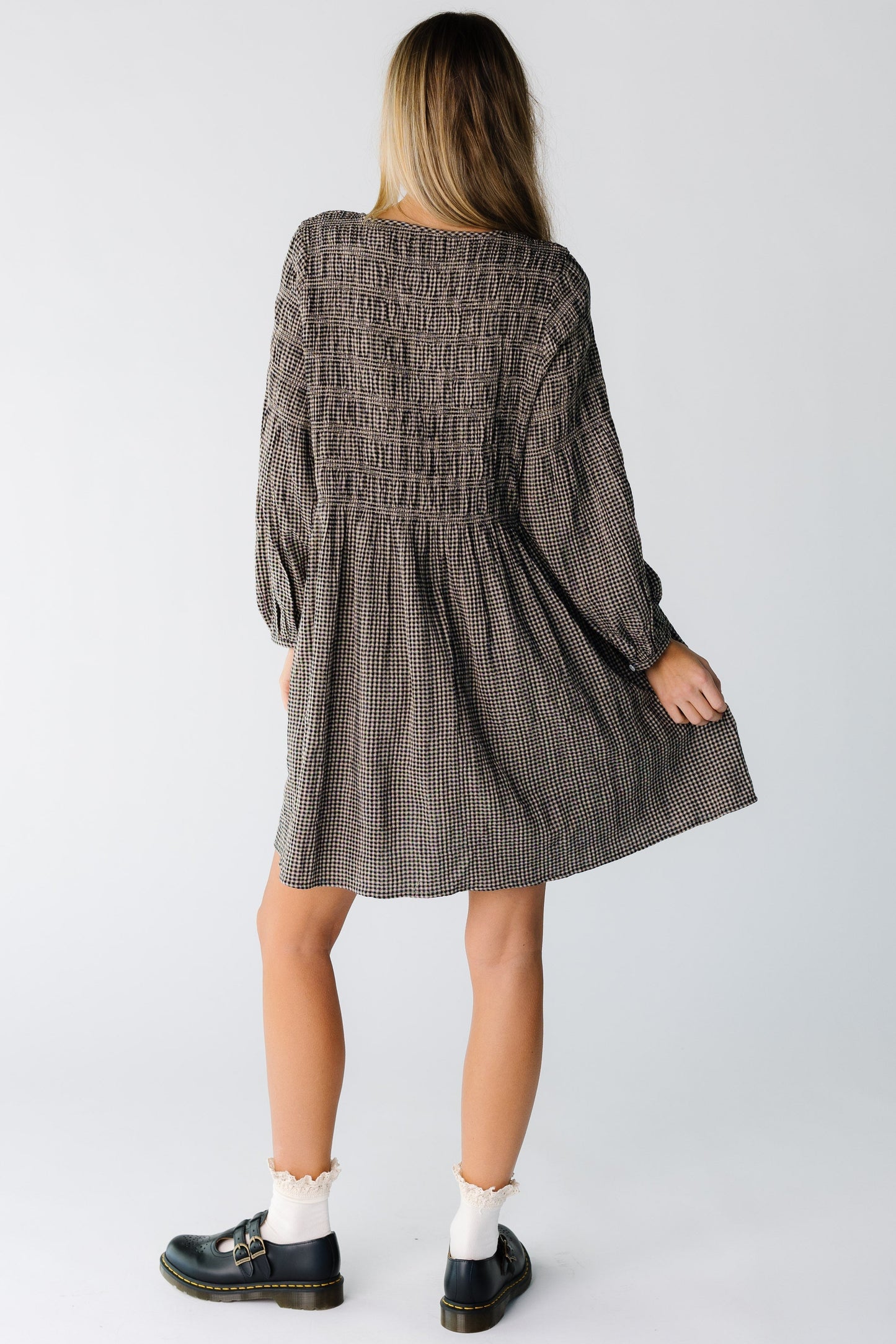 Back view of a woman wearing a knee length gingham dress with long sleeves