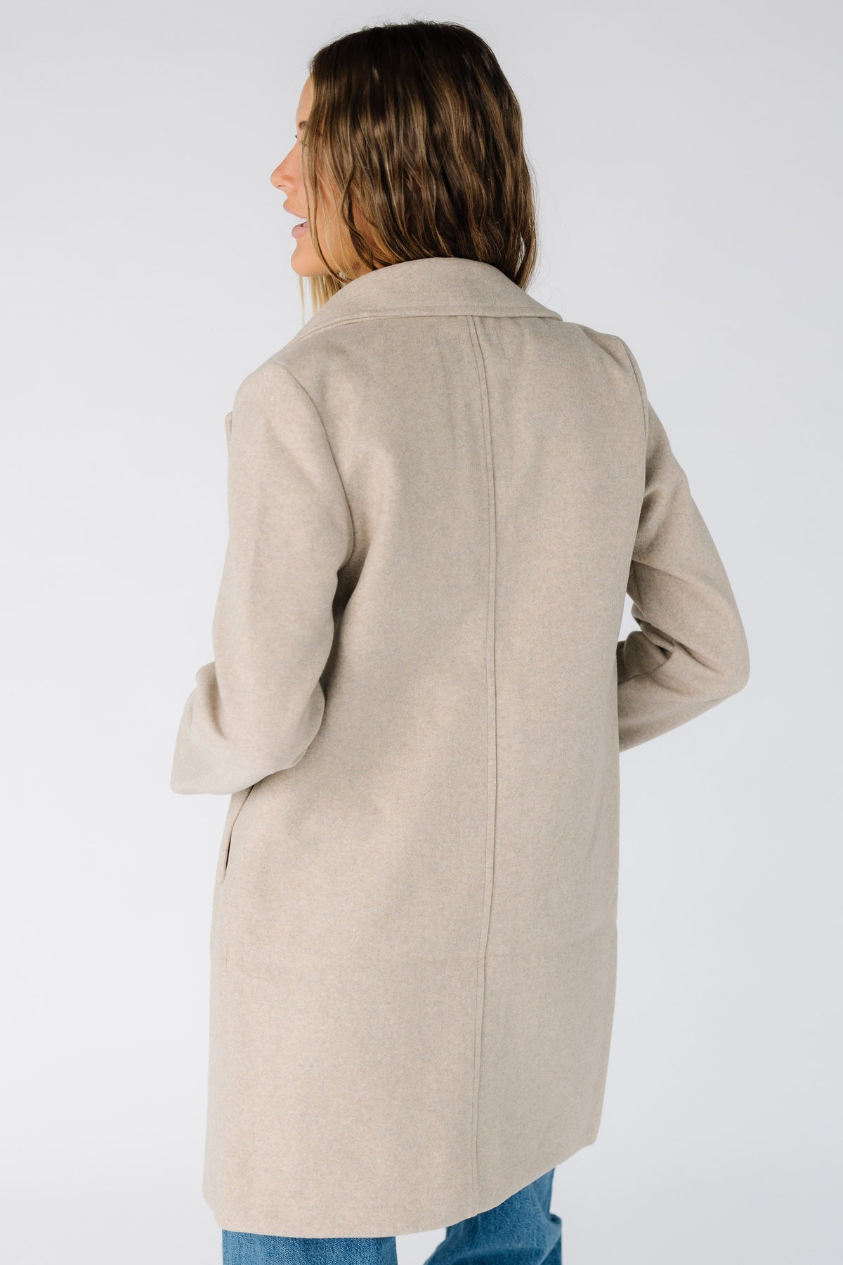Back view of a women wearing a long sleeve jacket with long sleeves in oatmeal tan