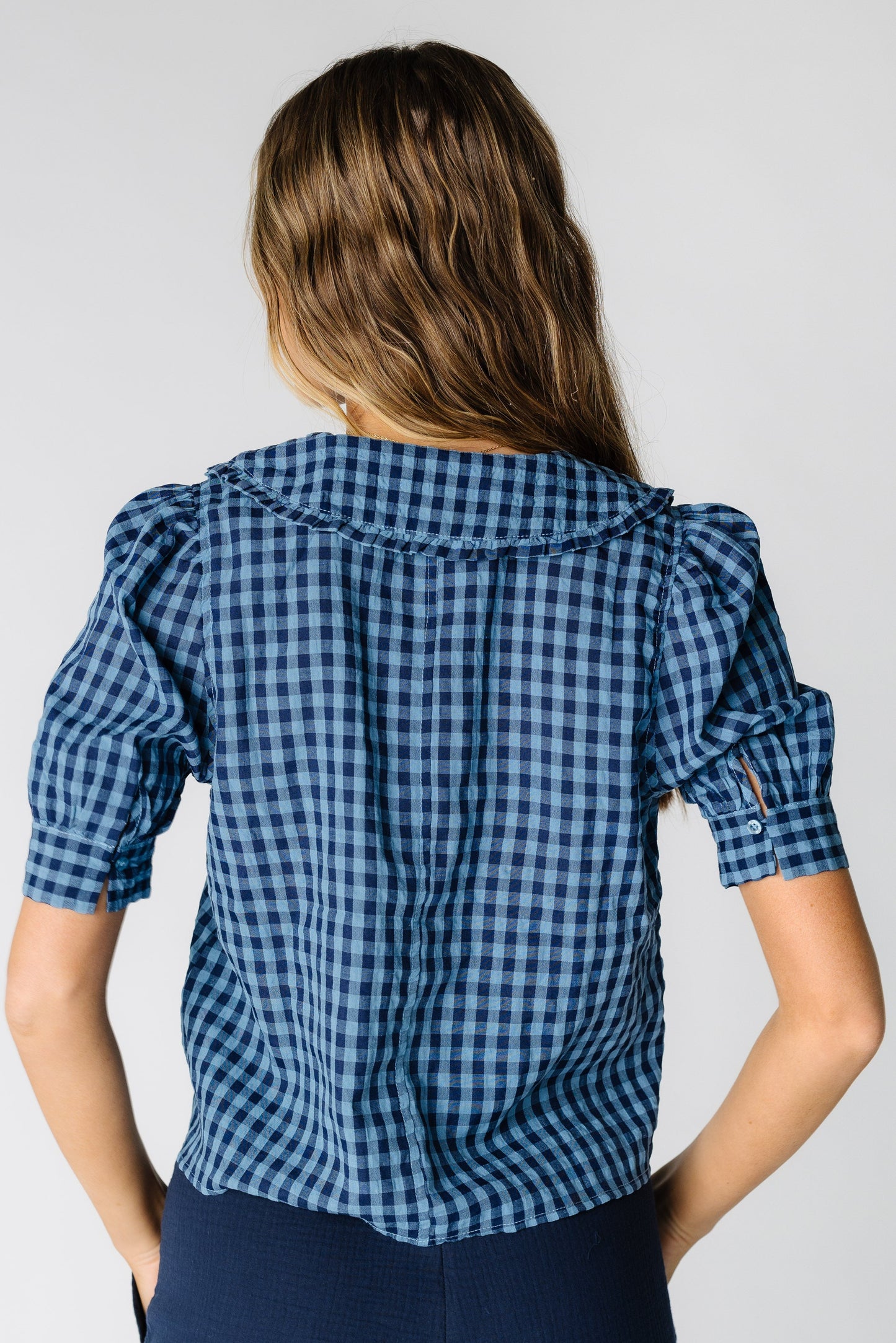 Back view of a woman wearing a nay gingham top with short puff sleeves