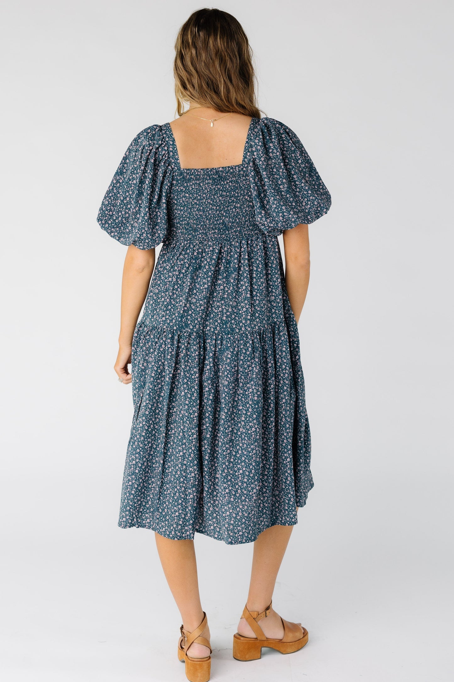 Back view of a woman wearing a blue floral dress with smocked back bodice and a full midi skirt