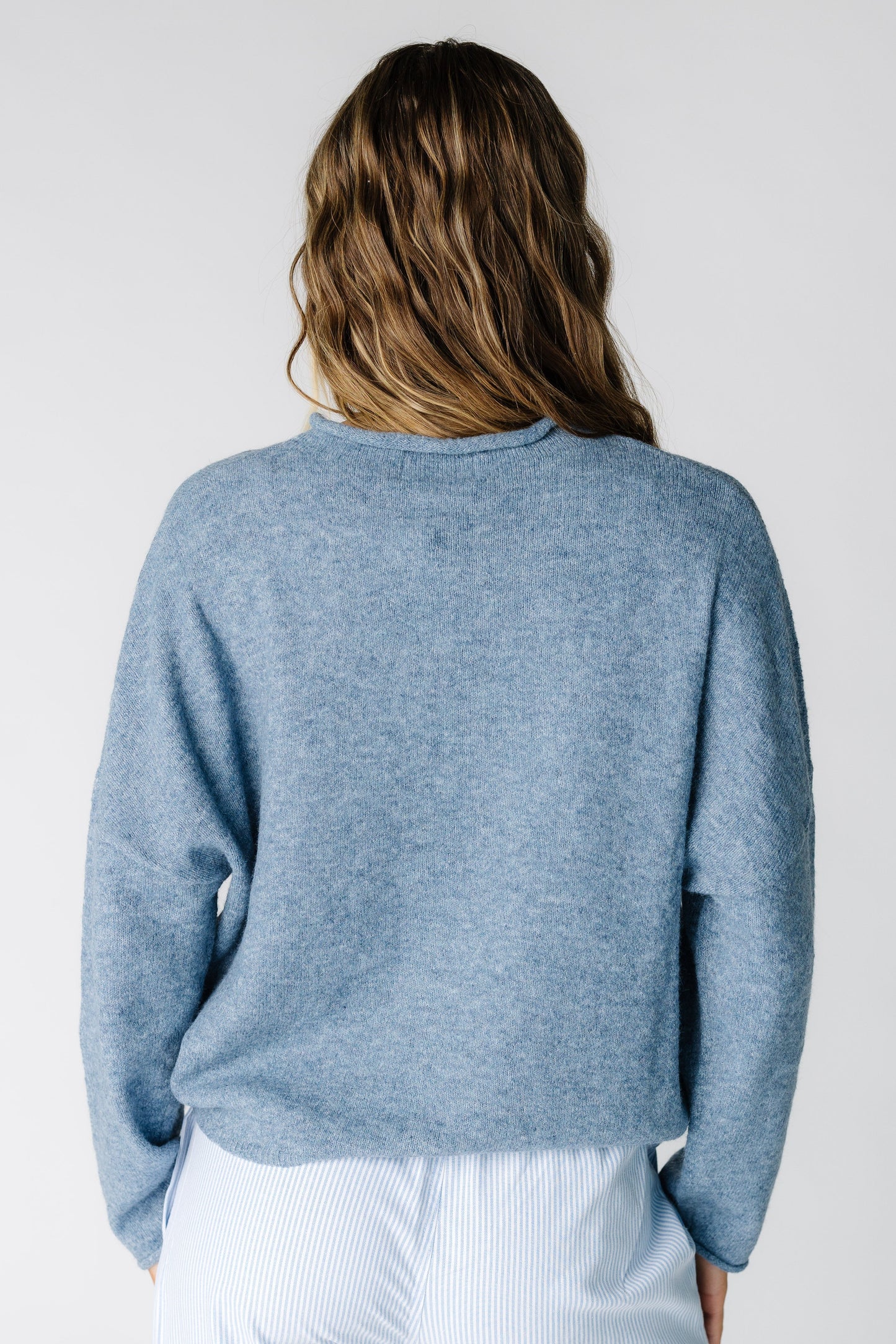 Back view of a woman wearing a dusty blue long sleeve sweater