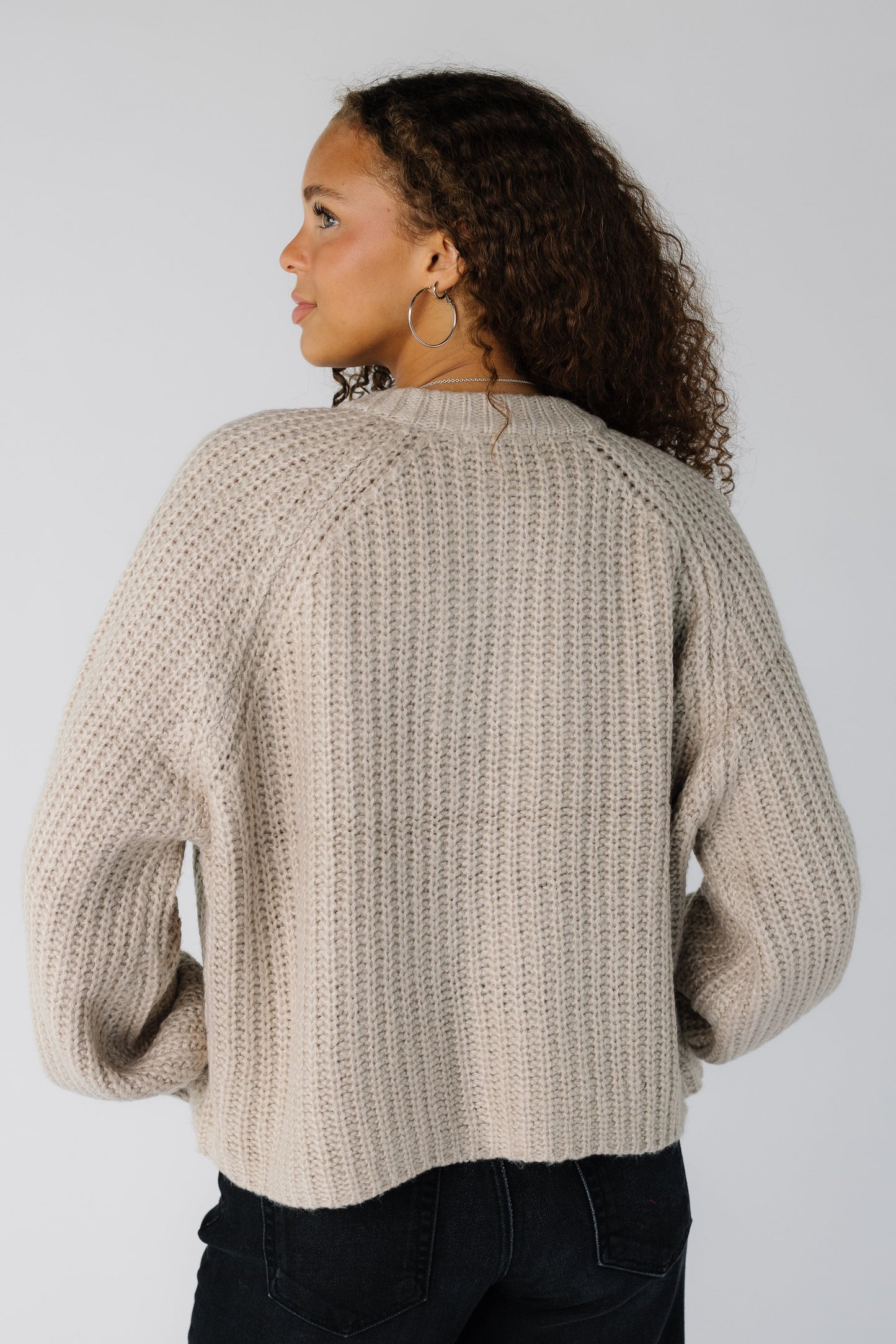 Back view of a teen girl wearing a loose fitting beige cardigan with long raglan sleeves
