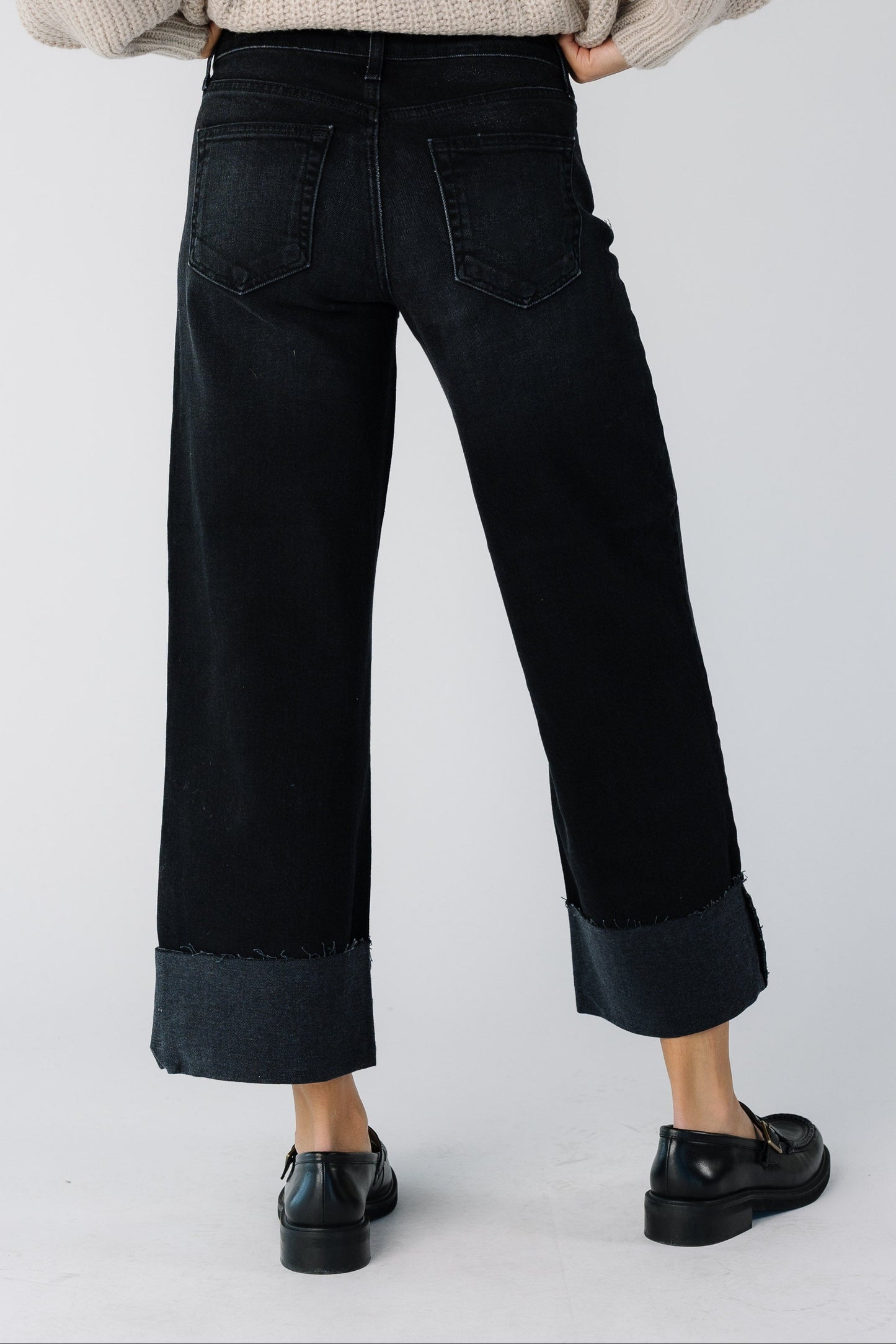 Back view of a teen girl wearing a pair of wide cut black jeans with a wide bottom cuff