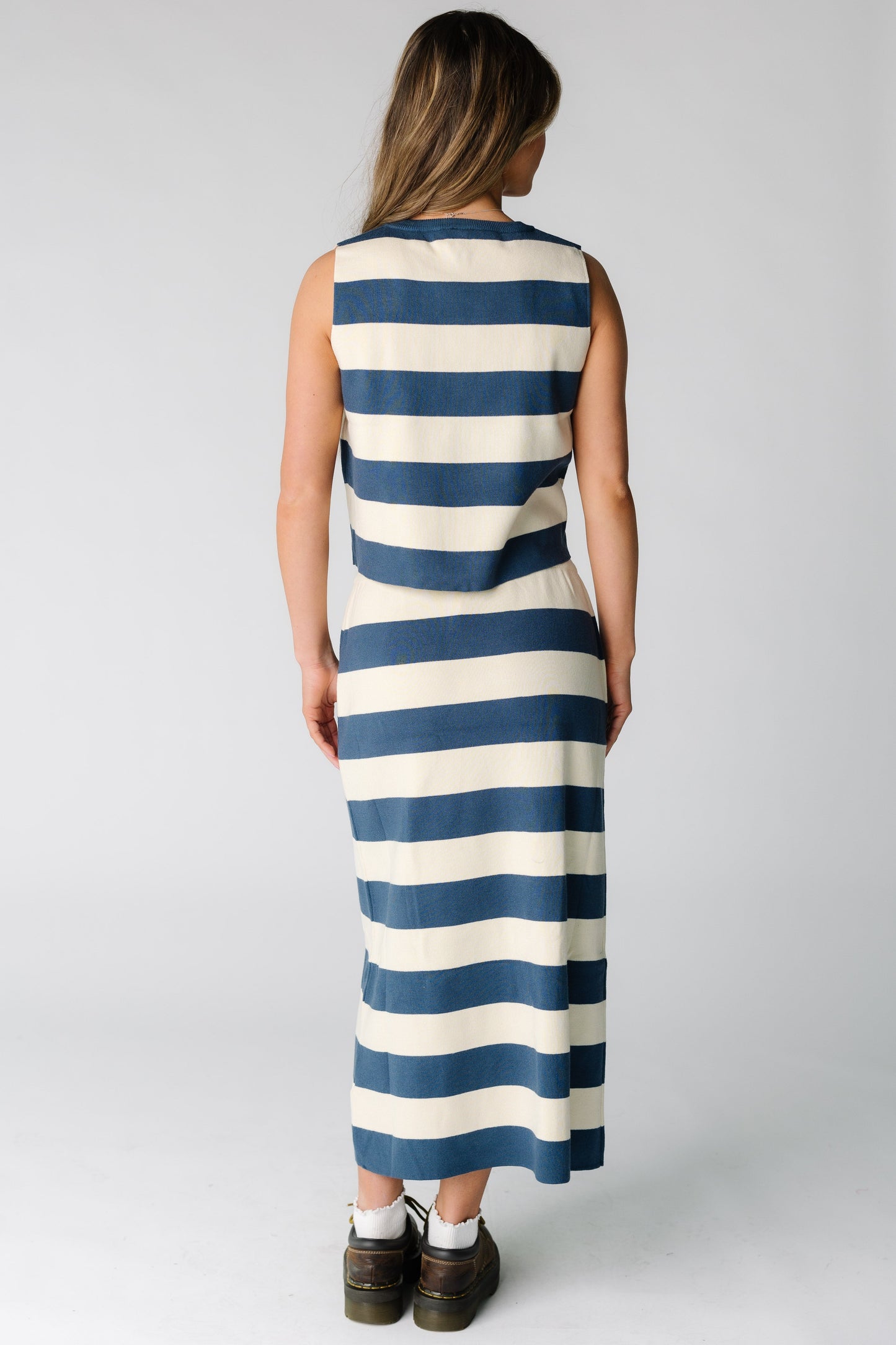 Back view of a woman wearing a blue and cream wide stripe skirt and top set with a midi skirt and sleeveless top.
