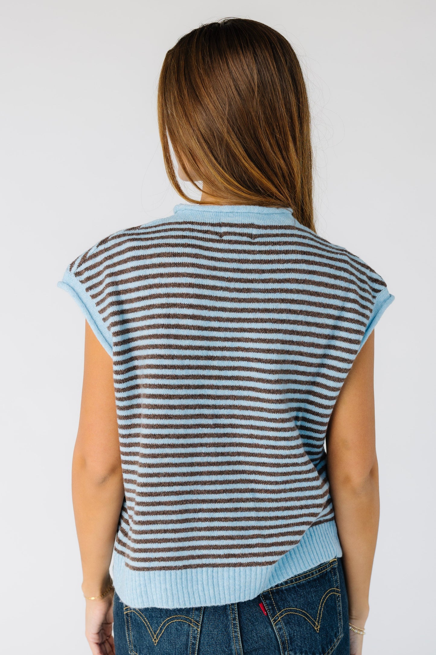 Bac view of a woman wearing a light blue and brown stripe sweater vest.