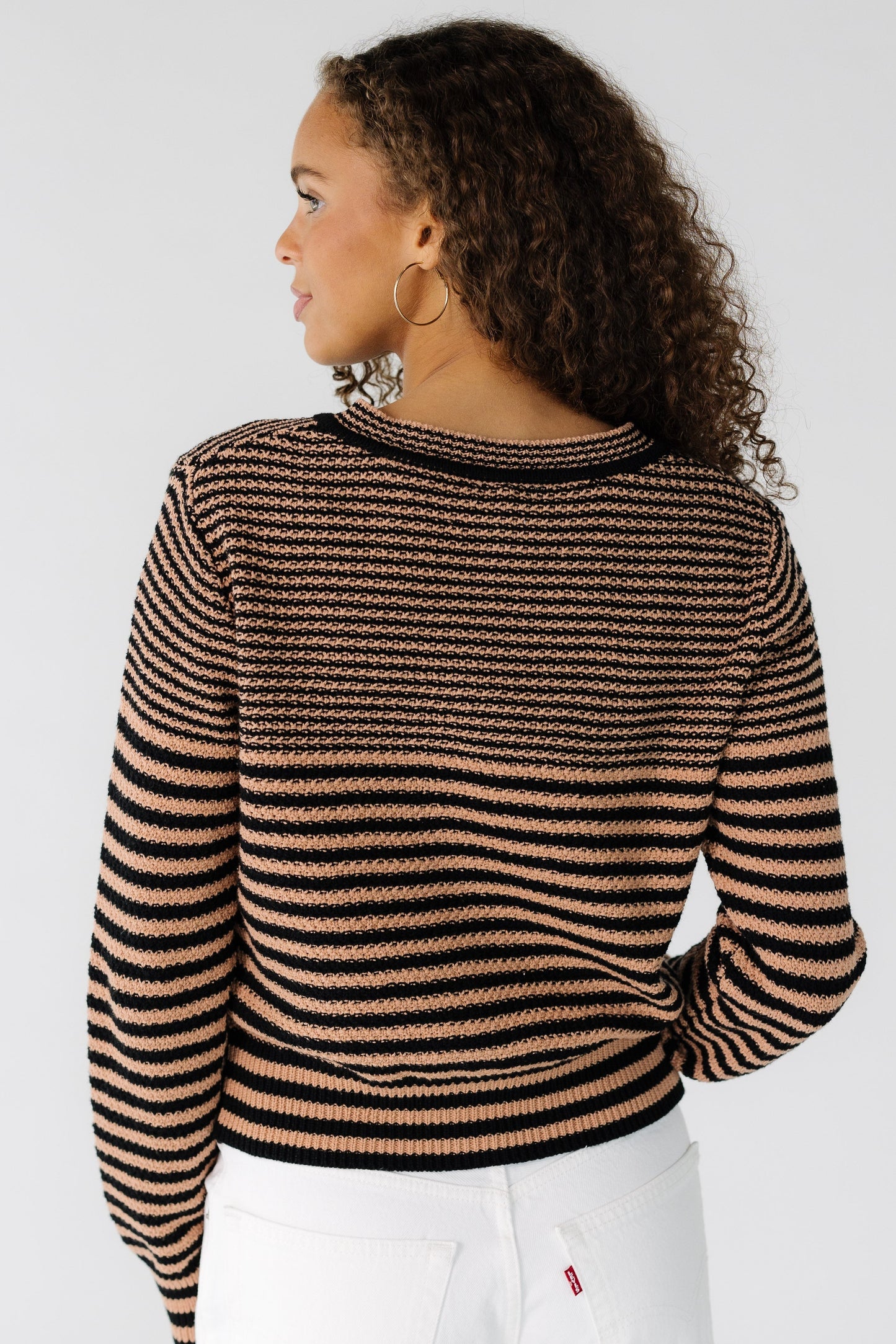 Back view of a teenage girl wearing a taupe & black stripe cardigan with long sleeves.