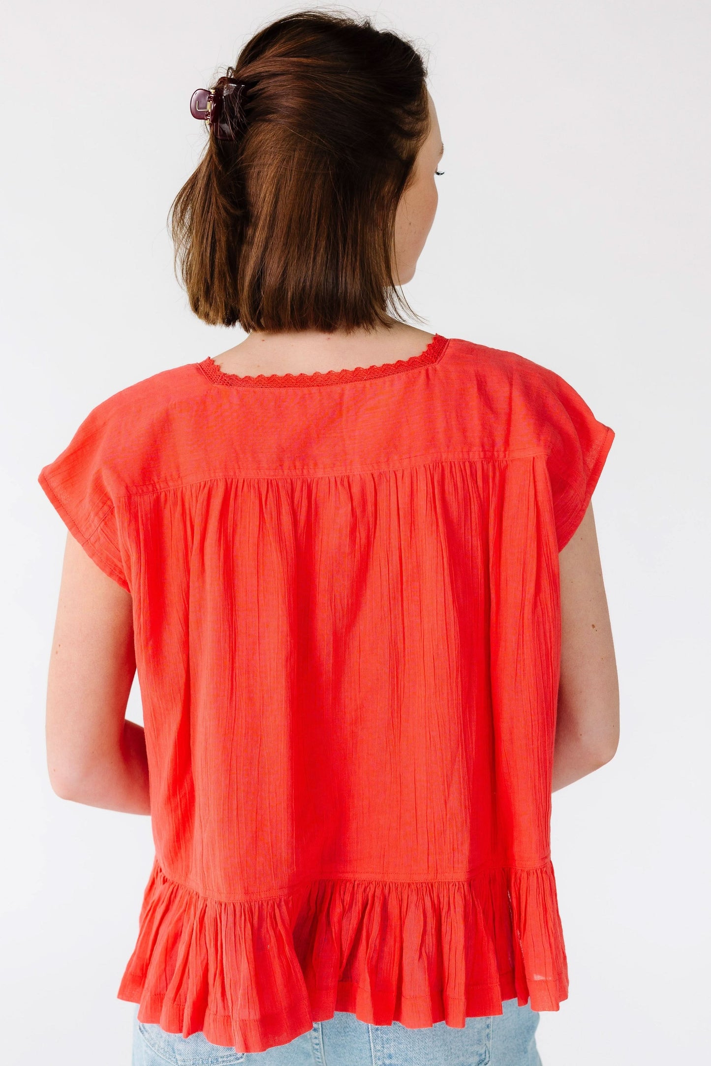 Back view of ayoung woman wearing a loose fitting red blouse with a wide bottom ruffle, and short cap sleeves.