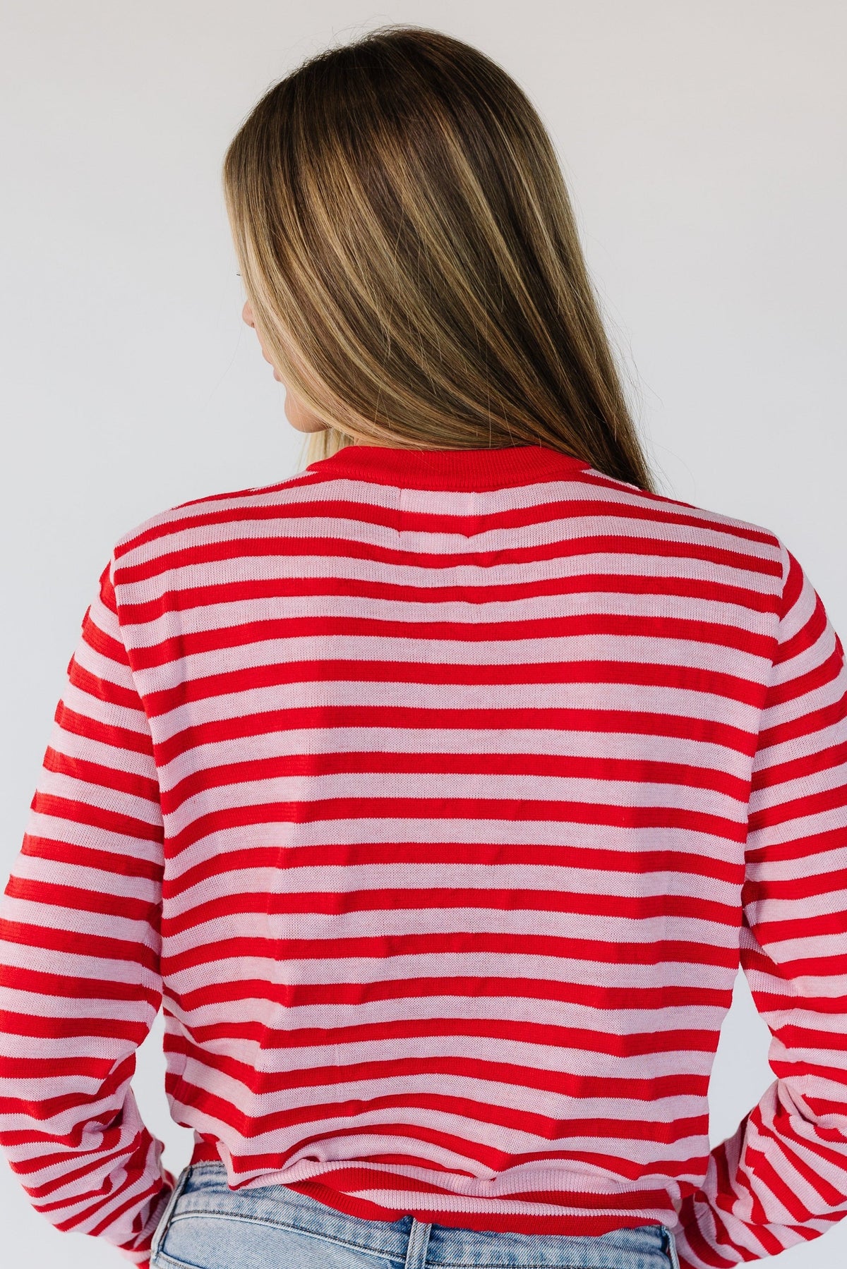 Back view of a woman wearing a red and light pink stripe cardigan.