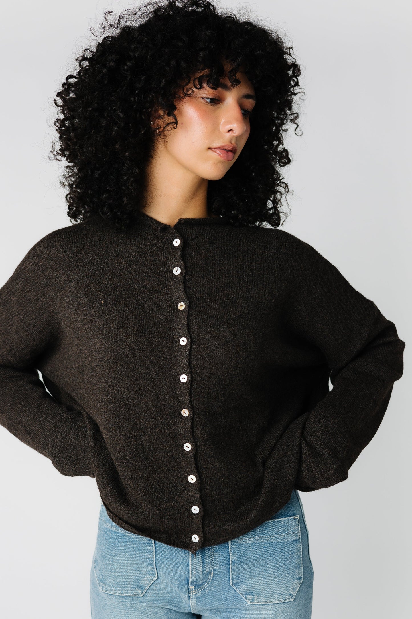 A woman wearing a brown cardigan sweater with contrasting buttons