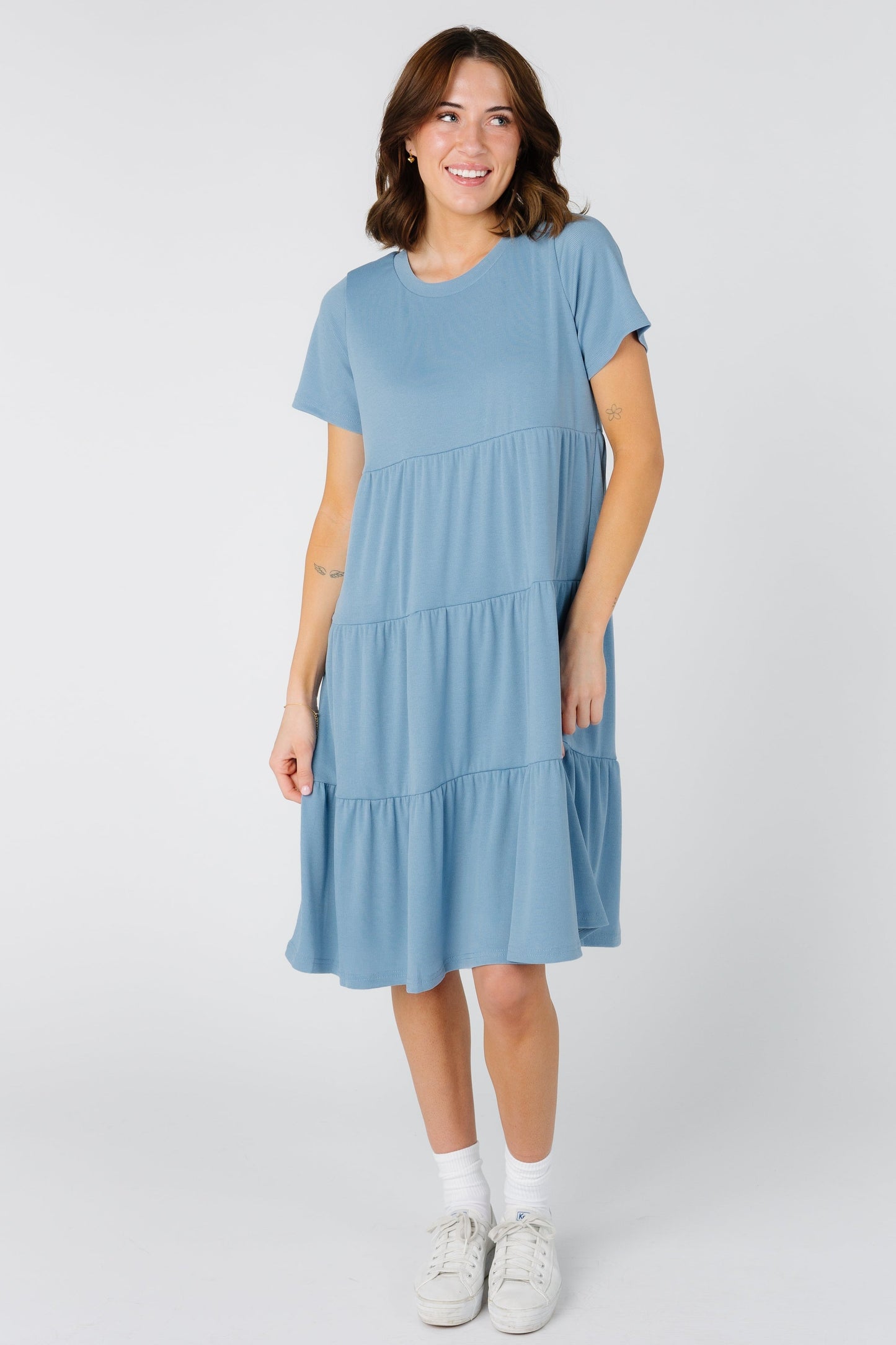 A woman wearing a dusty blue tiered dress with short sleeves