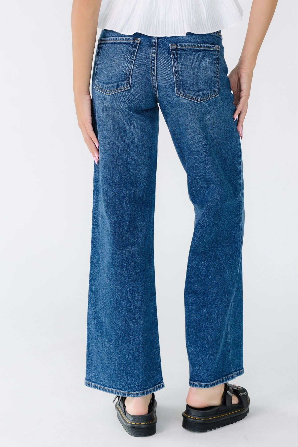 Back view of a young woman wearing a pair of dark denim wide leg jeans with sewn hems and mid rise waist.