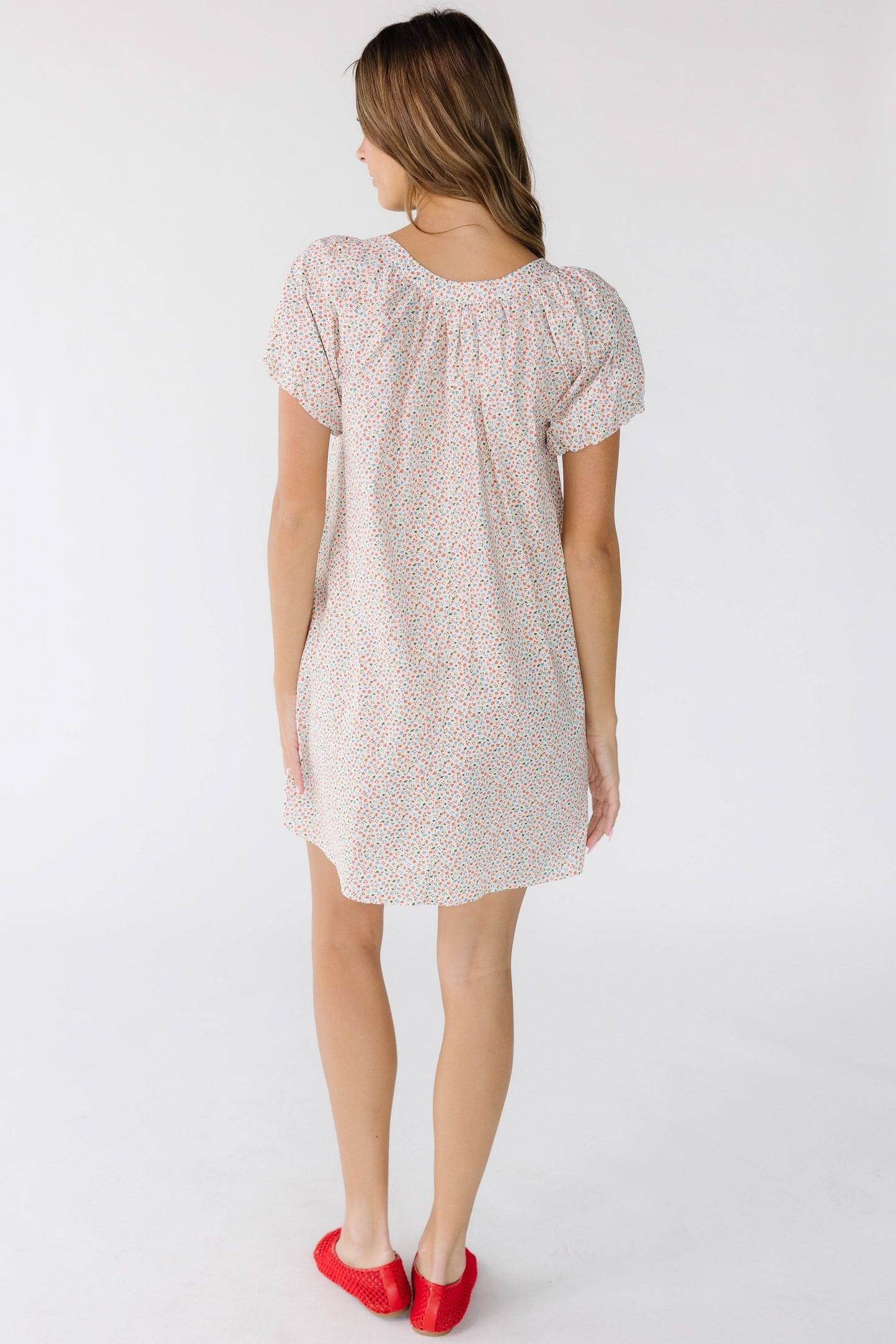 Back view of a woman wearing a white floral, short dress with puff sleeves.
