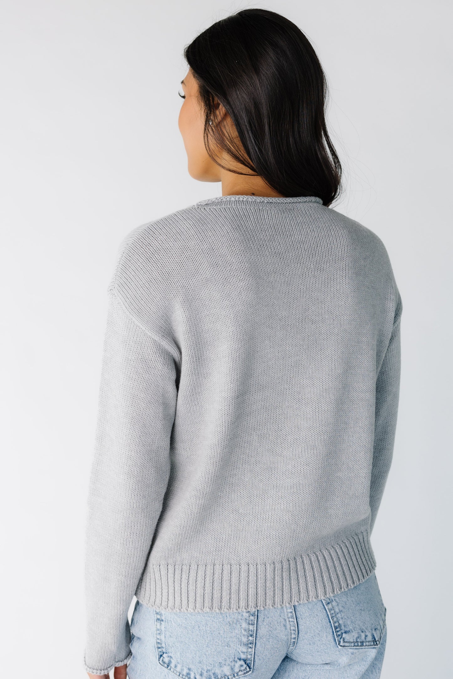Back view of a young woman wearing a grey long sleeve sweater.