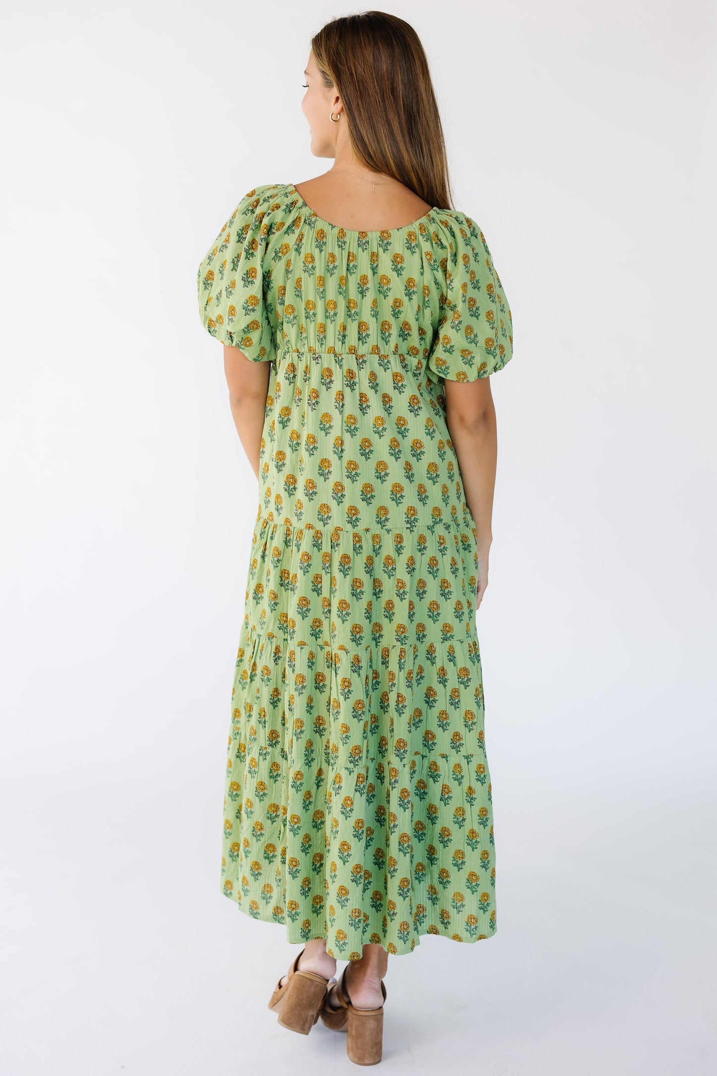 Back view of a woman wearing a green midi dress with short full sleeves and a back slight scoop neckline.