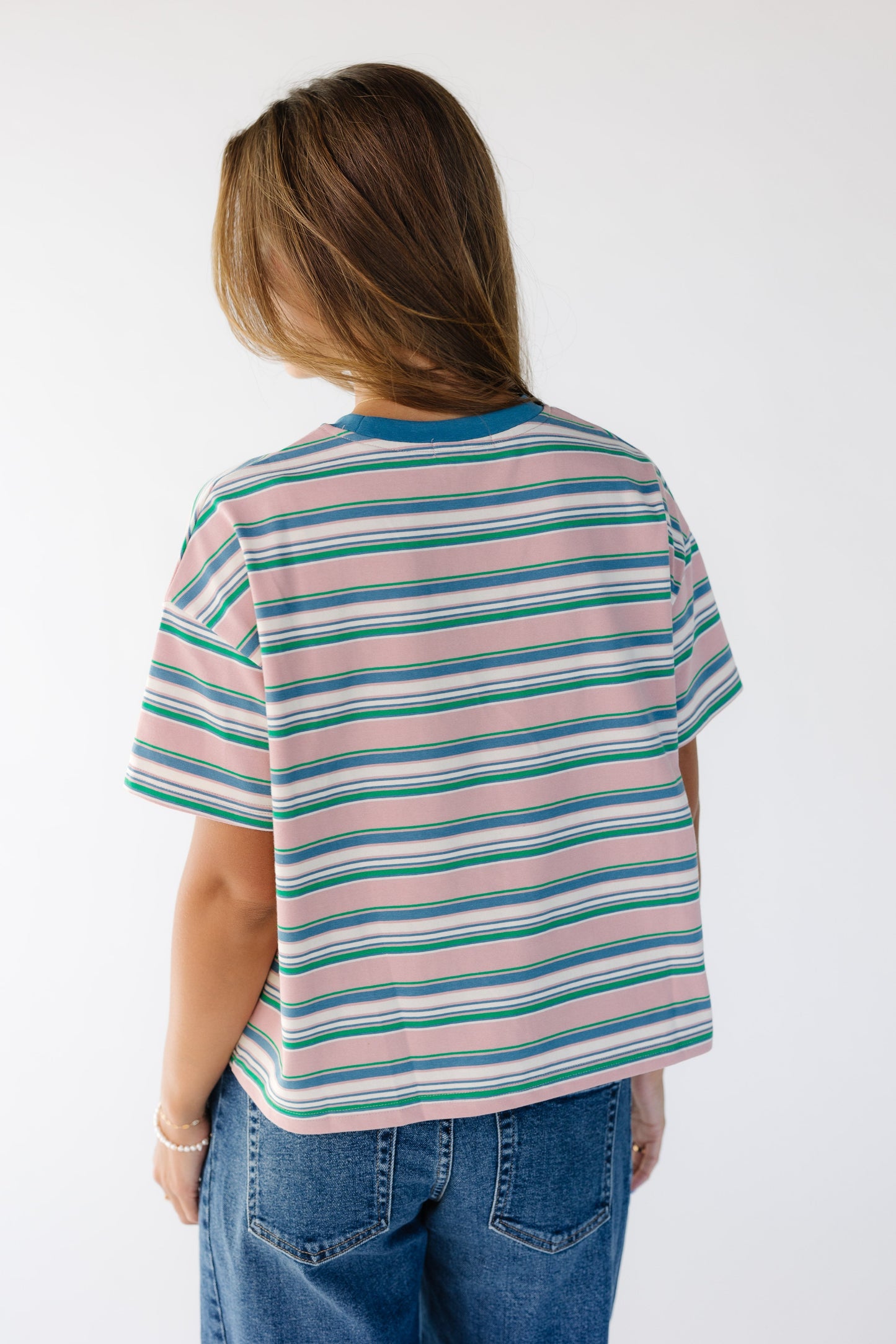 Back view of a woman wearing a loose fitting multicolor stripe tee with short sleeves.