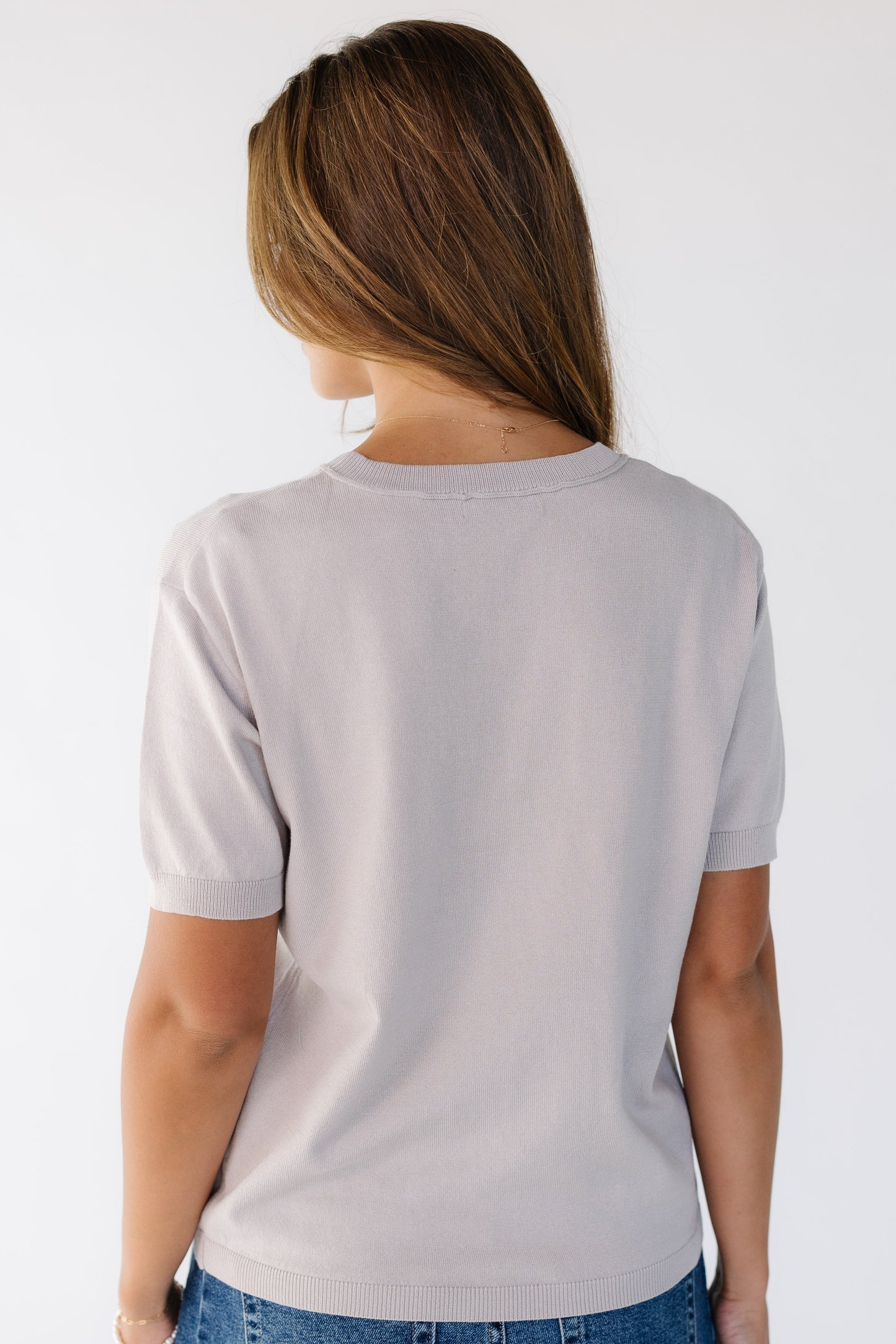 Back view of a young woman wearing a soft lightweight sweater with short sleeves with a crew neckline.