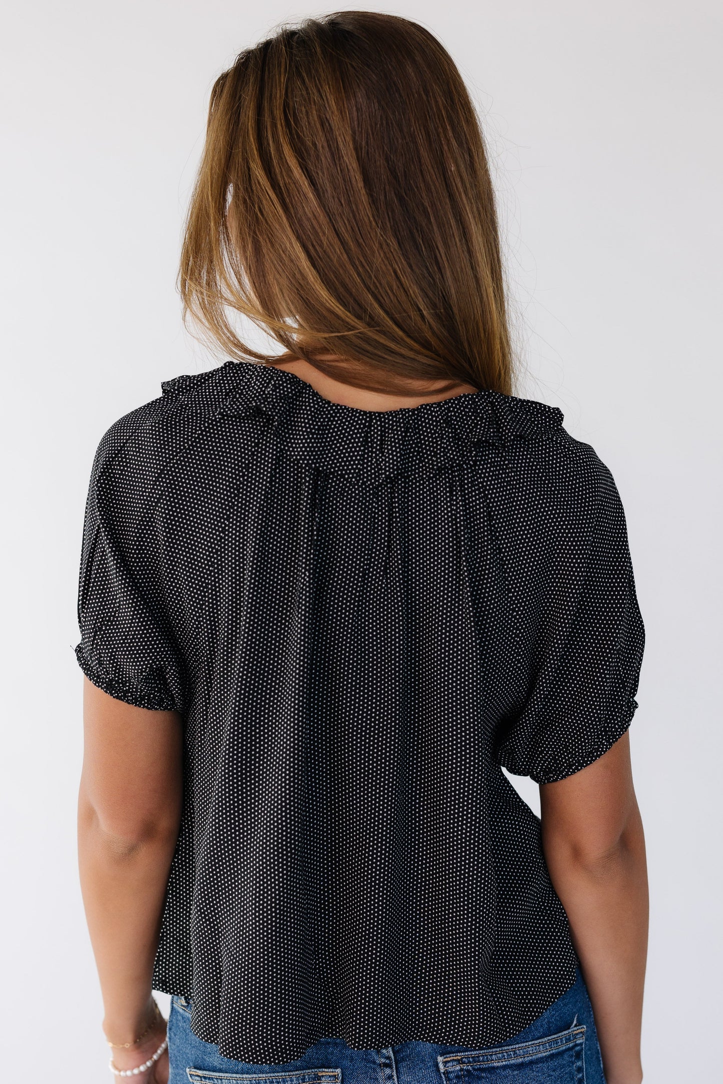 Back view of a woman wearing a loose fitting black polka dot top with short puff sleeves.