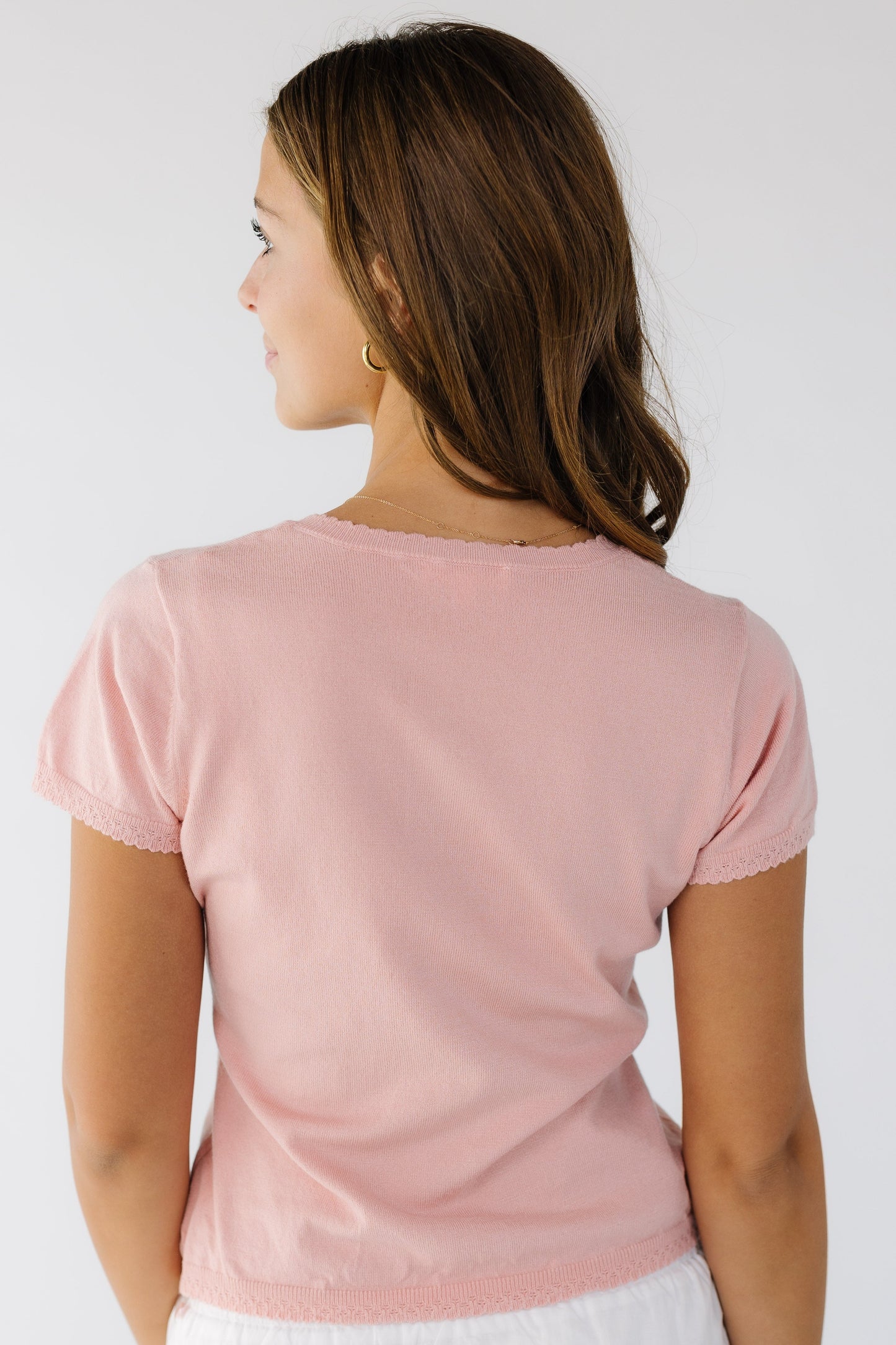 Back view of a woman wearing a pink knit top with scallop hems and short sleeves.