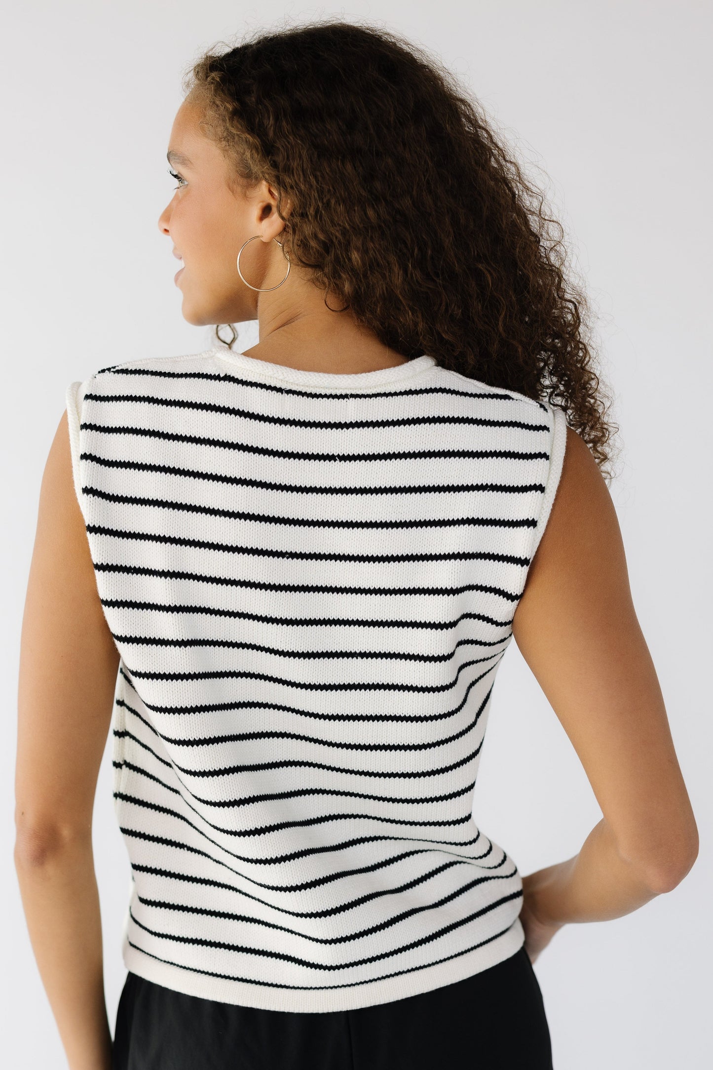 Back view of a teen girl wearing a white sweater vest with black stripes.