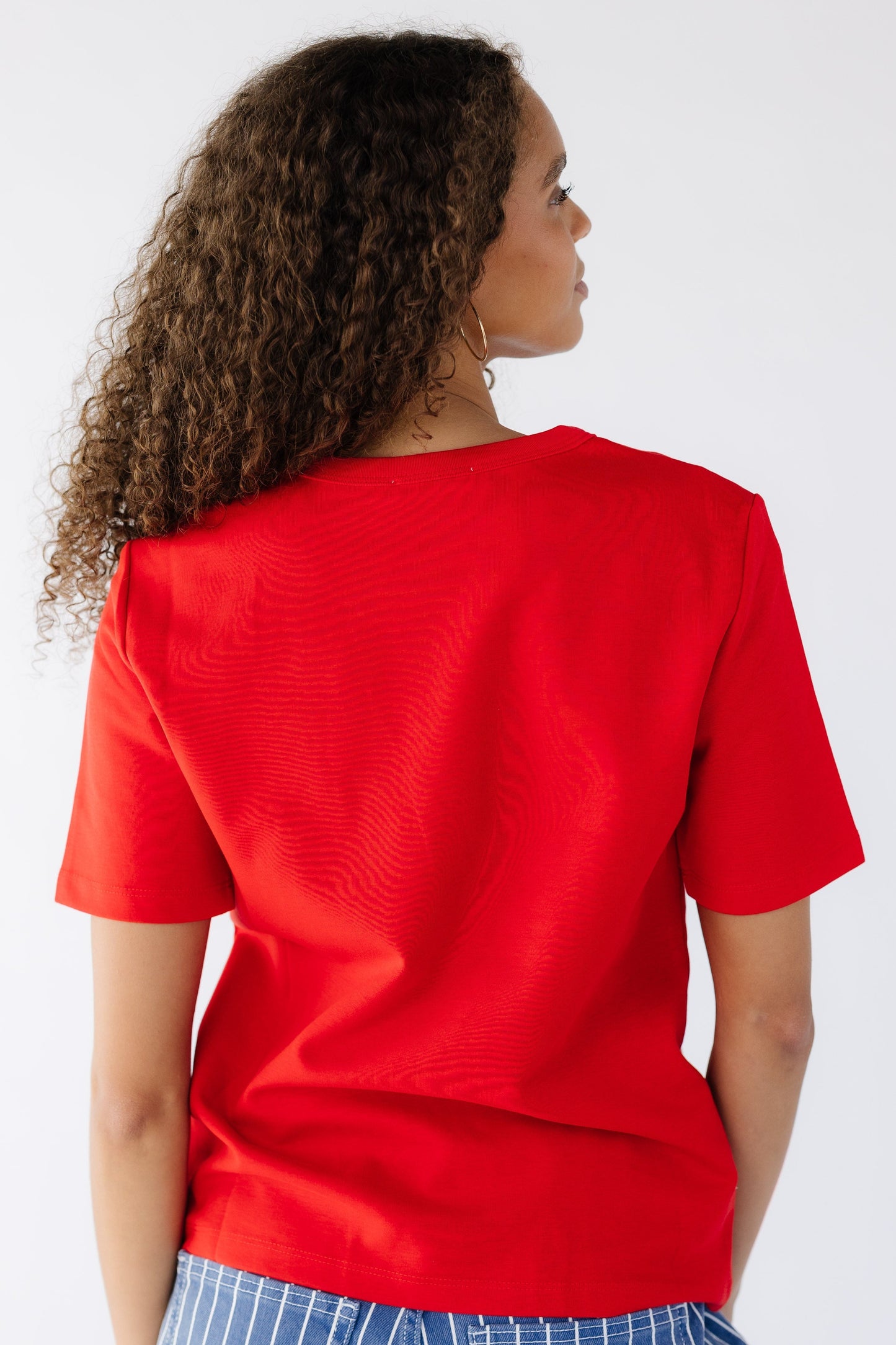 Back view of a teenage girl wearing a slightly loose fitting, short sleeve tee in red.