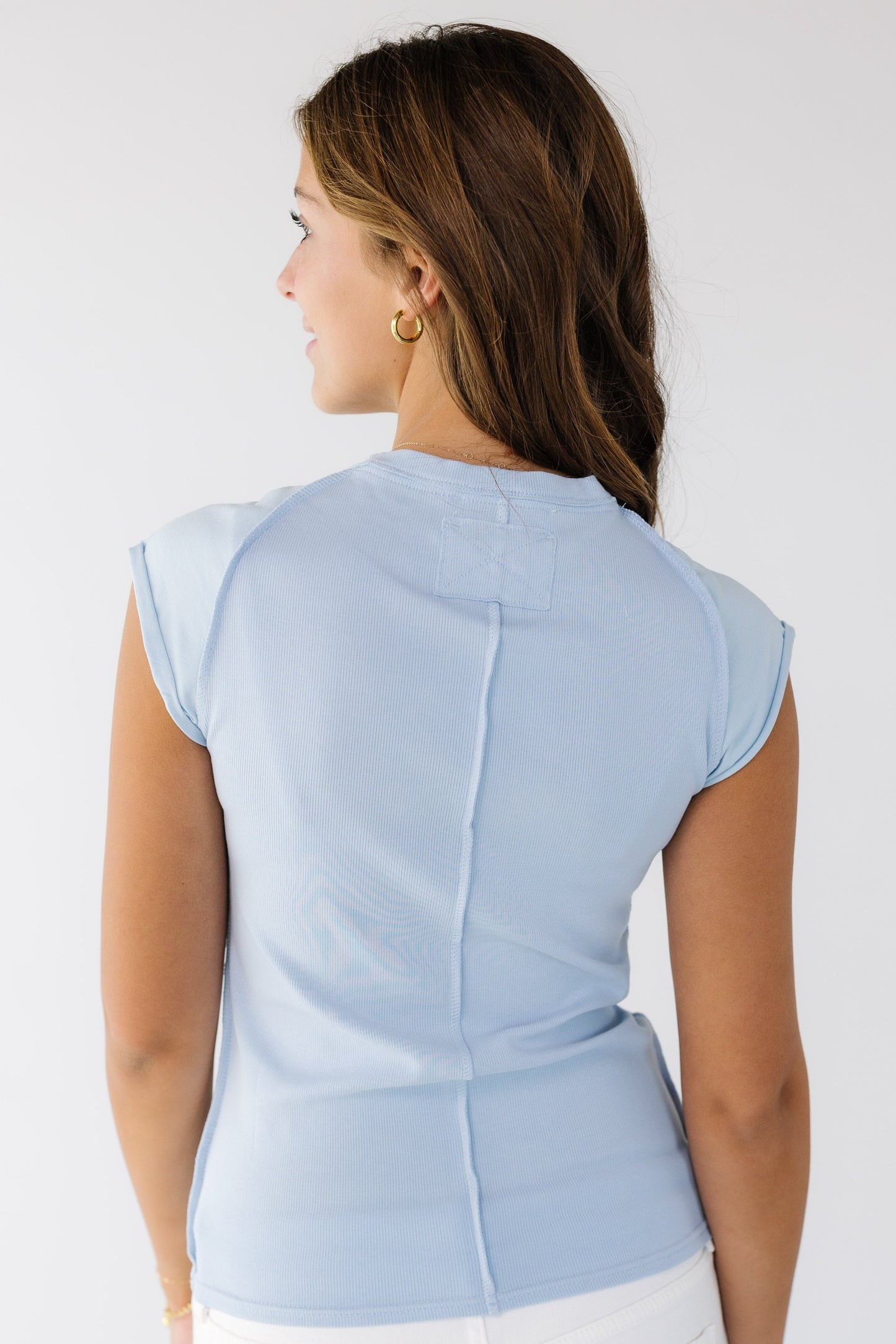 Back view of a woman wearing a light blue close fitting top with exposed seams and raglan sleeves made of a smooth fabric.