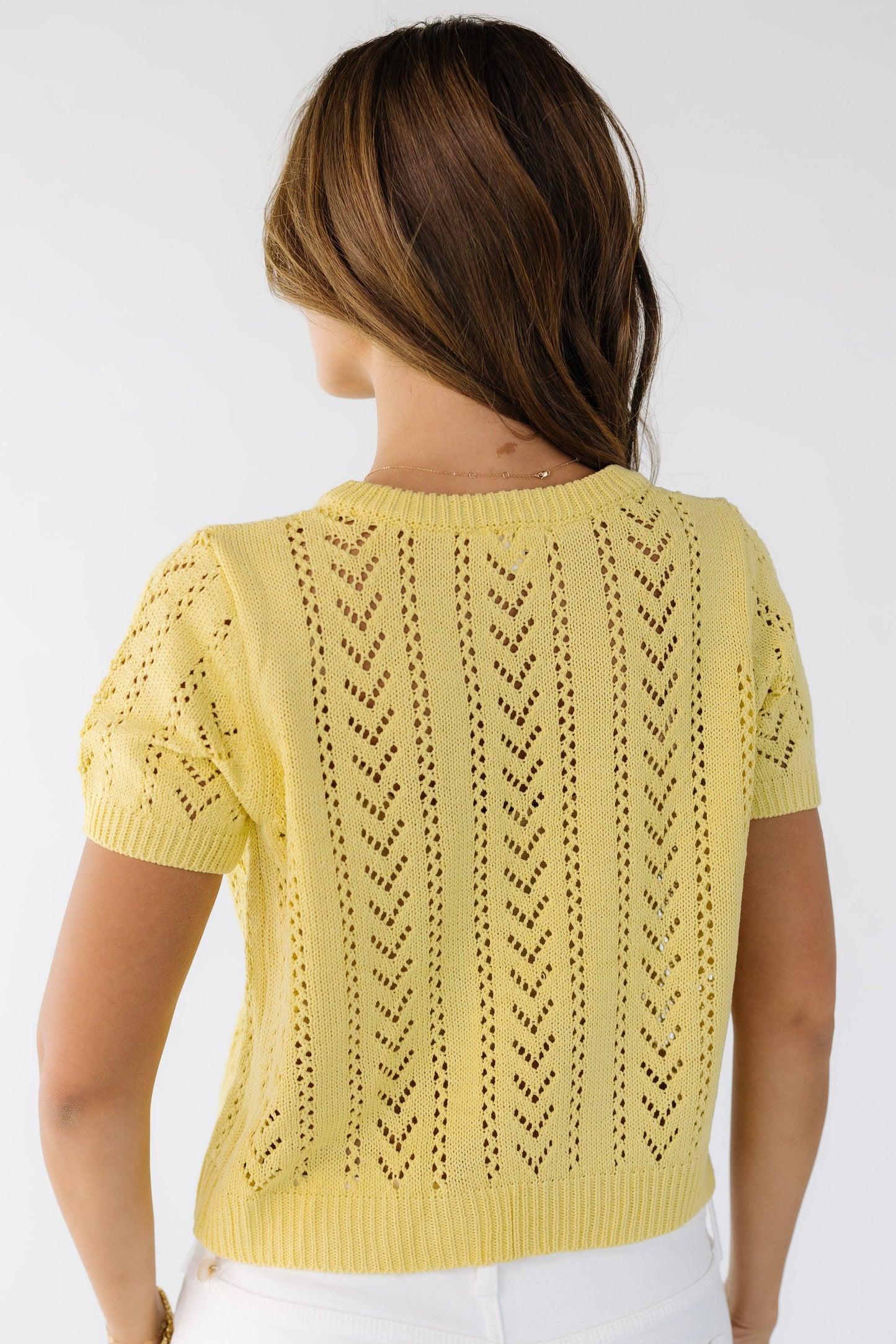 Back view of a woman wearing a lacey knit cardigan in yellow with short sleeves.