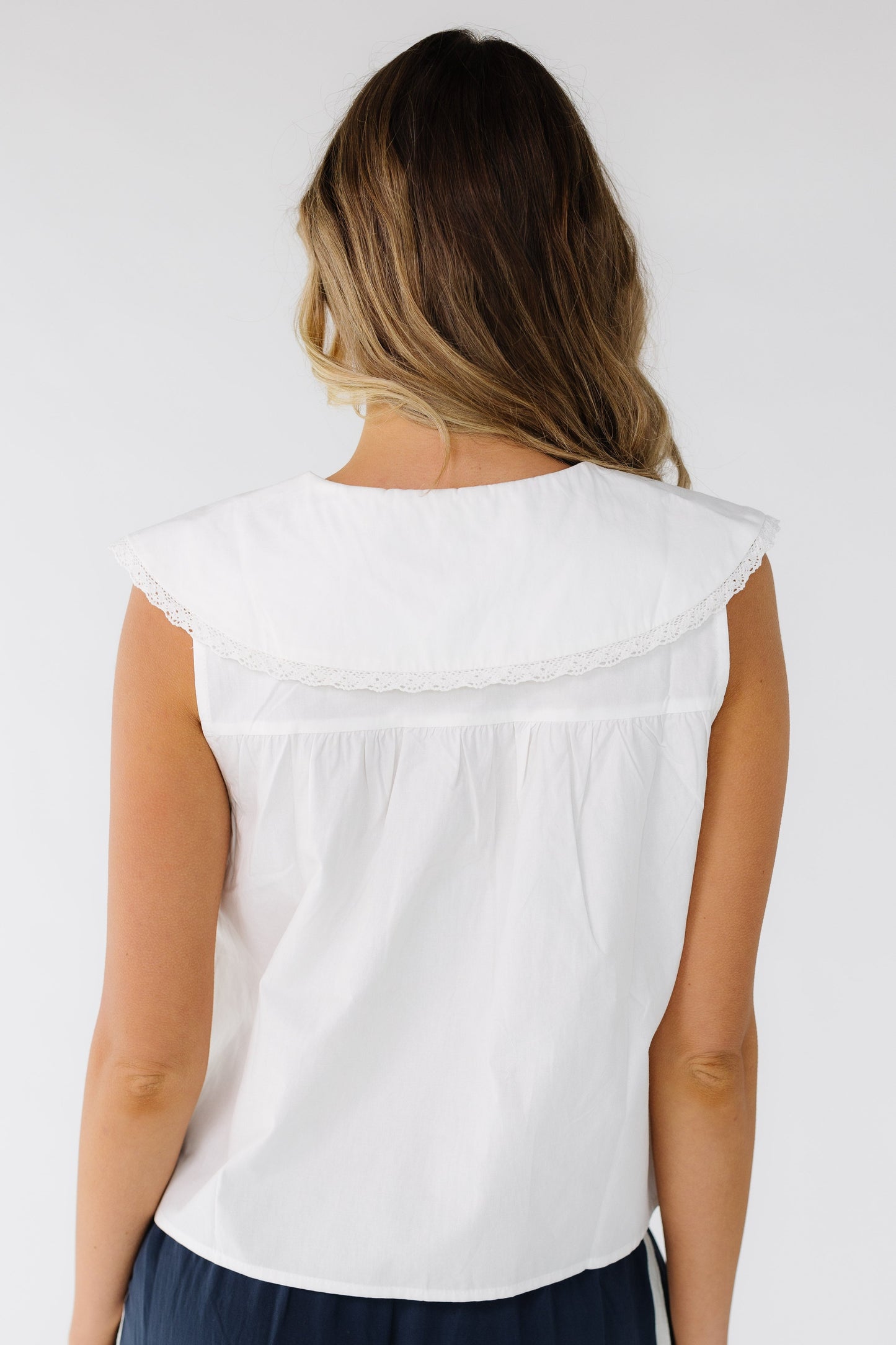 Back view of a young woman wearing a sleeveless white blouse with a wide lace trimmed collar.