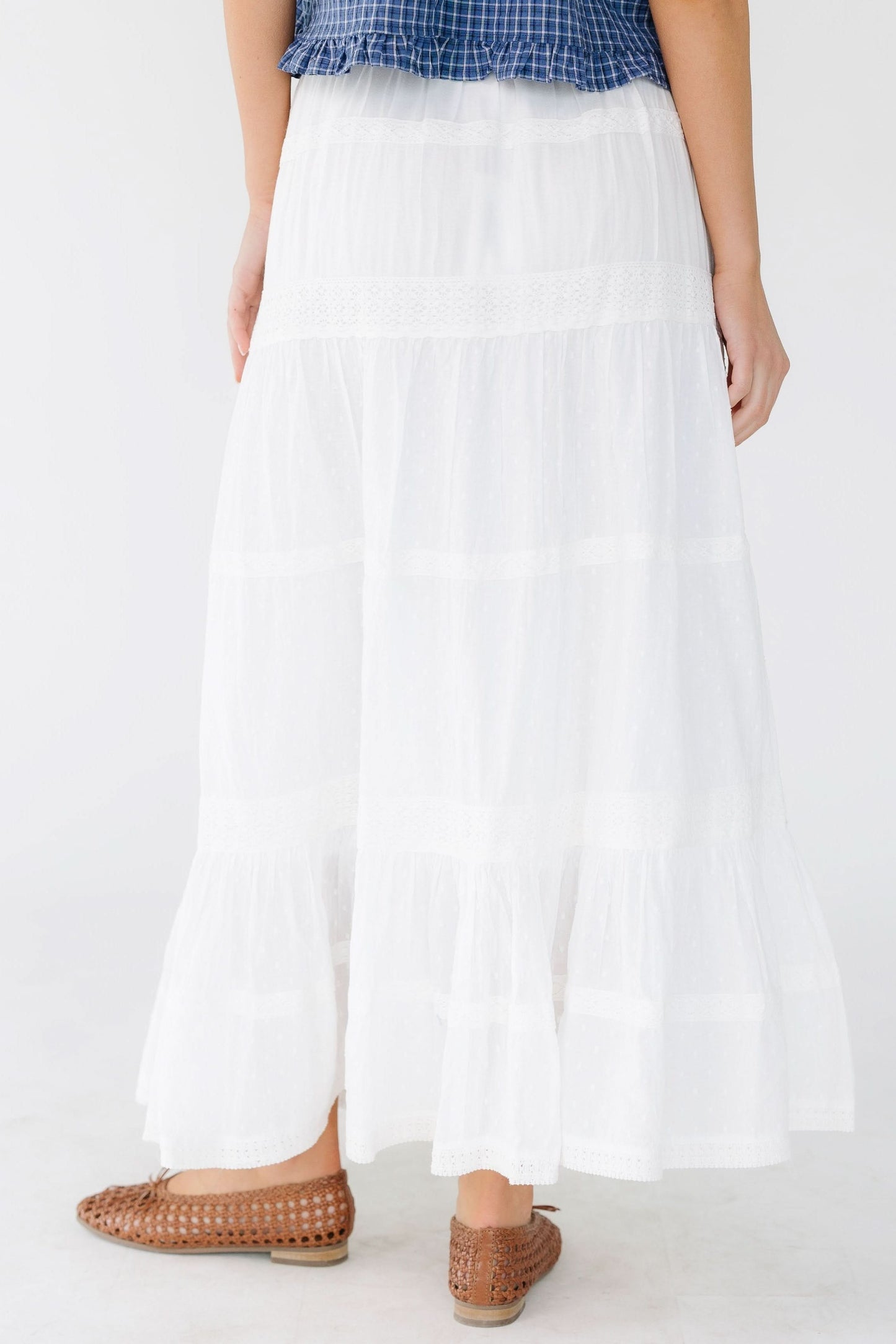 Back view of a woman wearing a white tiered and and lace trimmed midi skirt with an elastic waist.