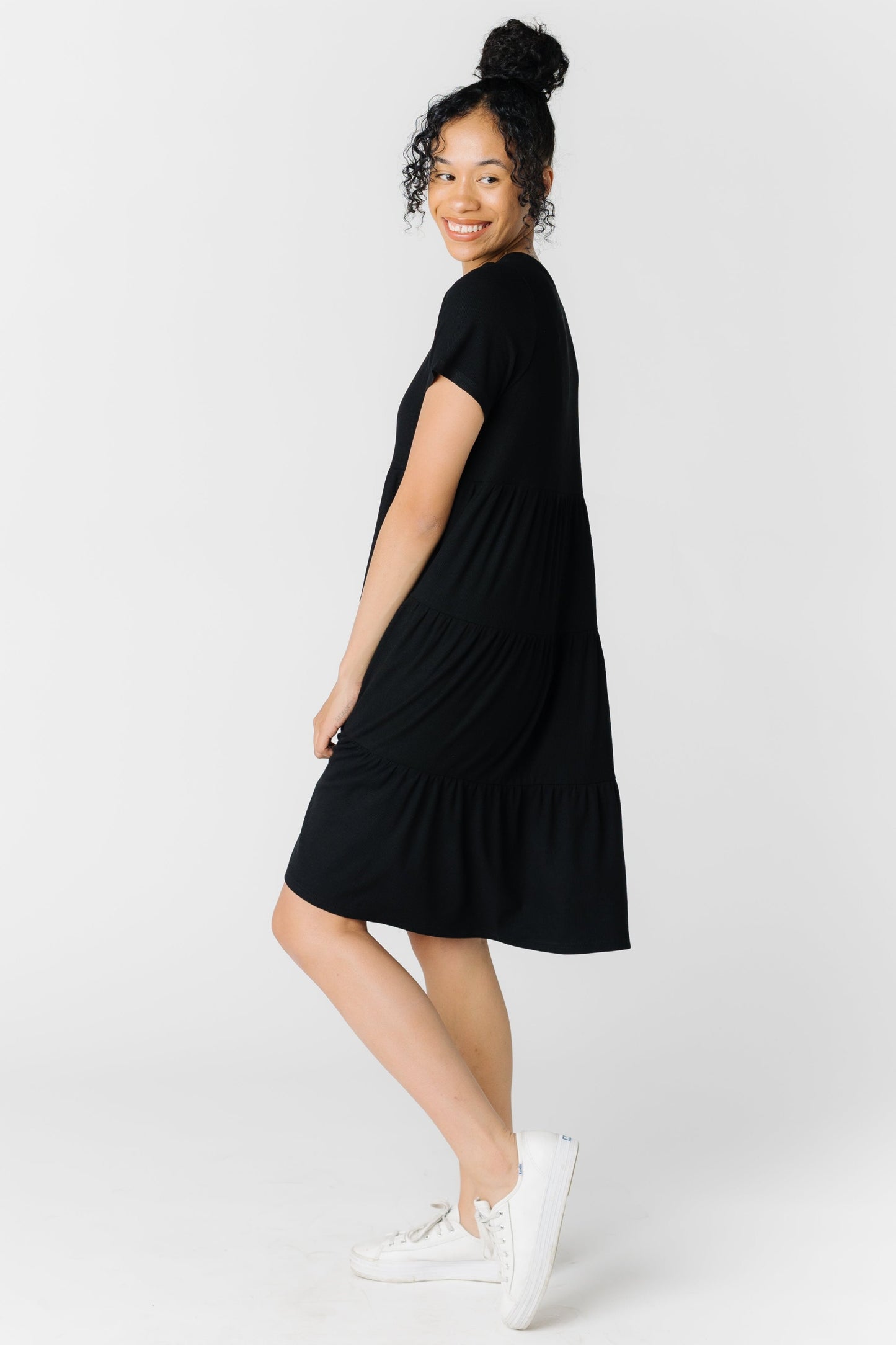 A woman wearing a black knee length tiered dress with short sleeves