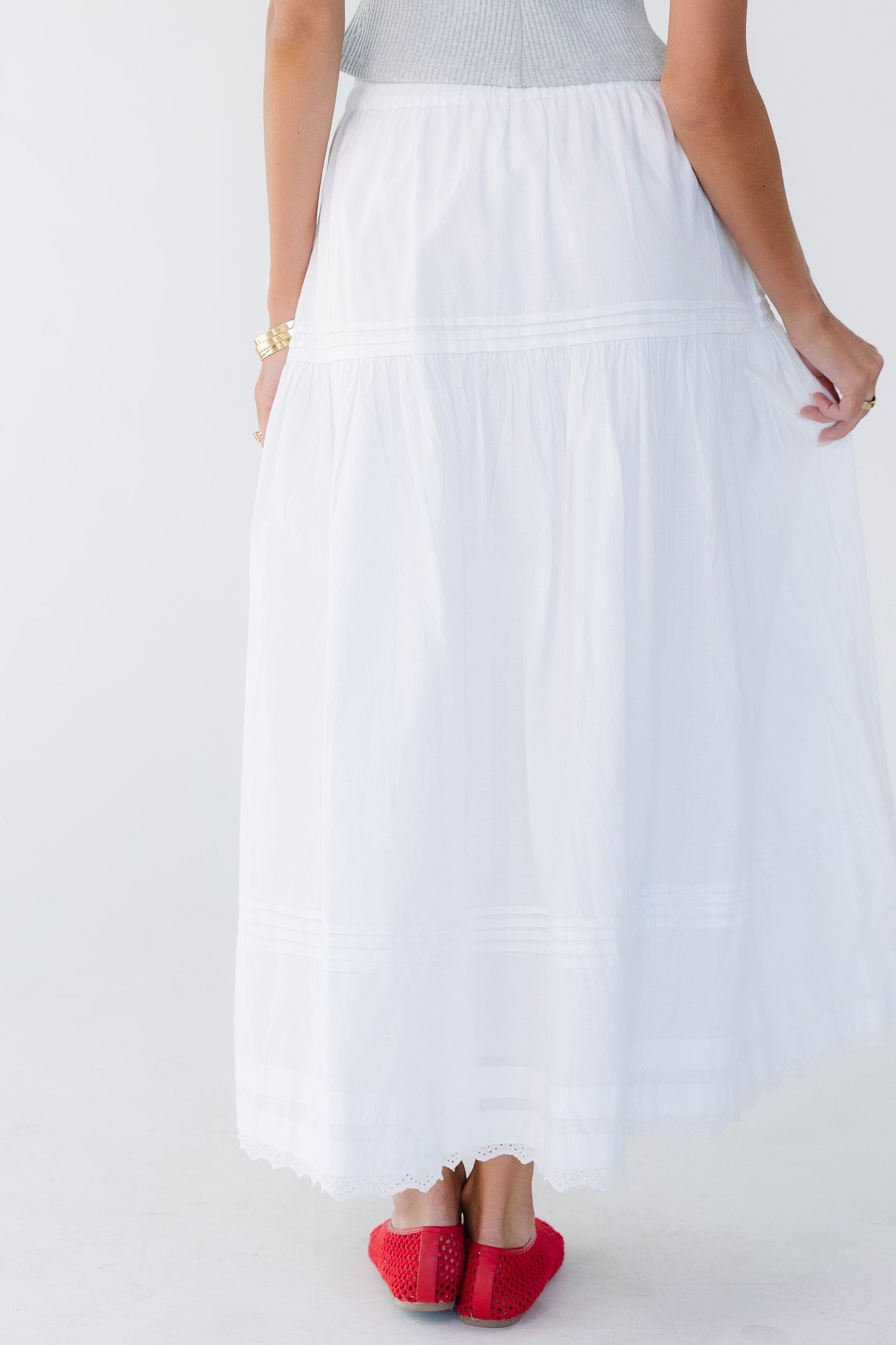 Back view of a woman wearing a white midi-maxi skirt with gathers, pleats and lace details.