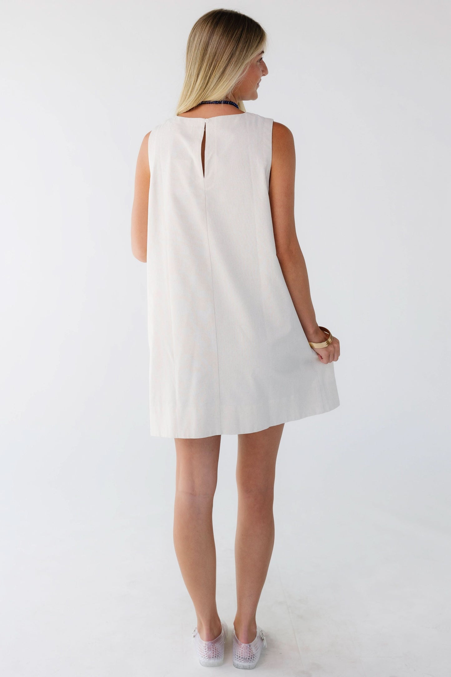Back view of a woman wearing a cream loose fitting sleeveless shift dress.