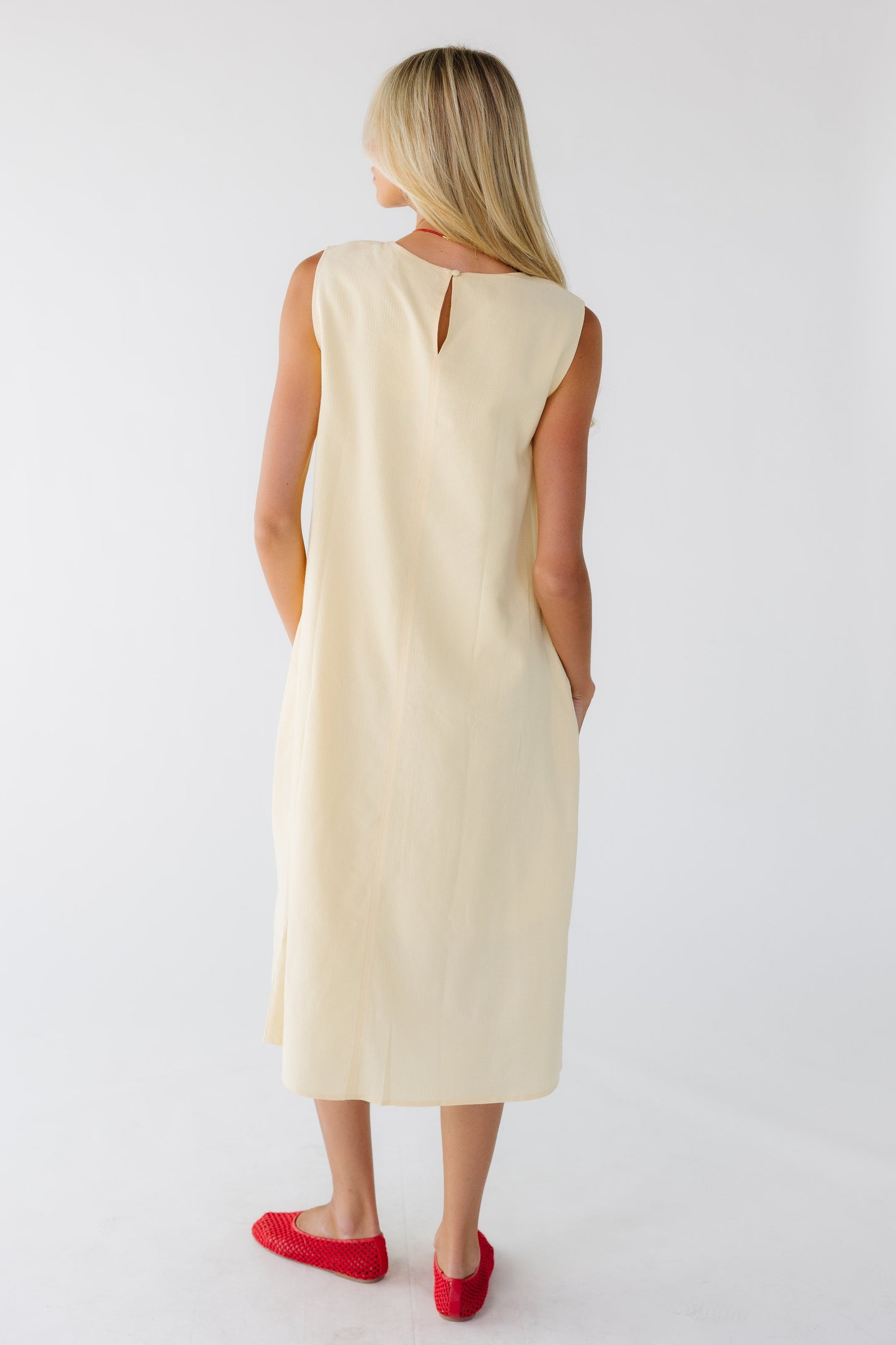 Back view of a woman wearing a yellow sleeveless midi dress with a back keyhole and button closure.
