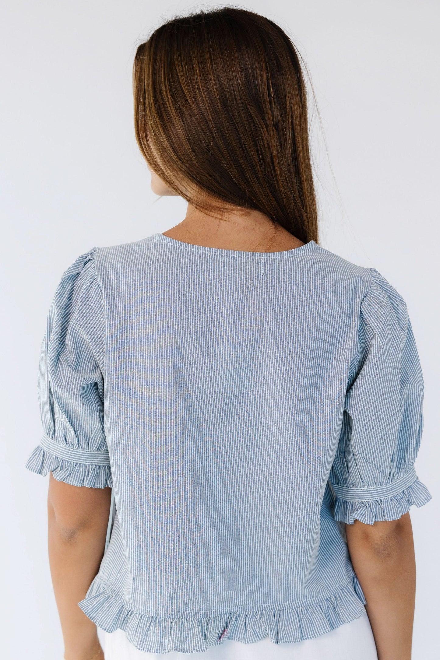 Back view of a young woman wearing a loose fitting blue & white stripe blouse with elbow length puff sleeves.