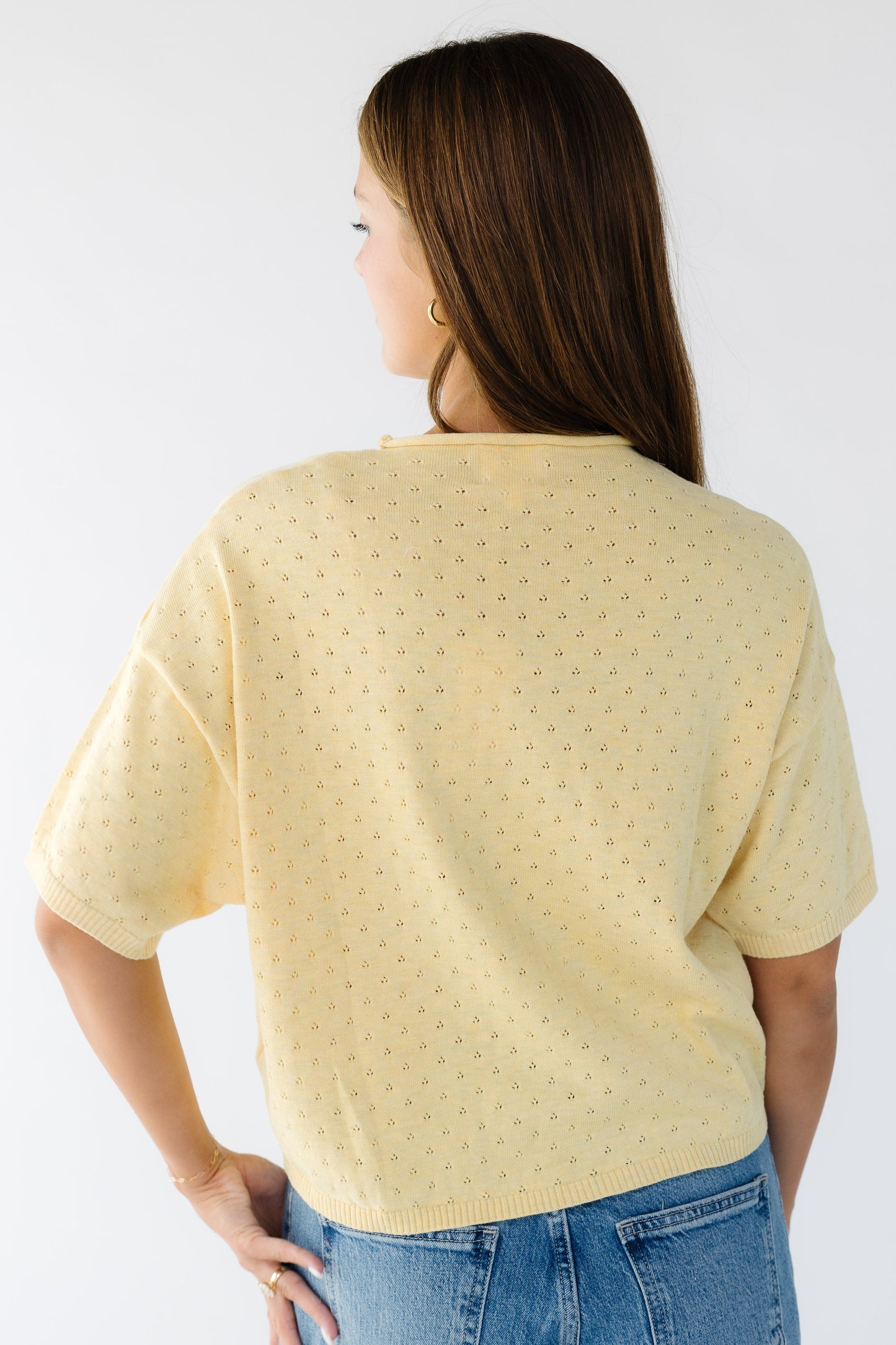 Back view of a woman wearing a light yellow pointelle sweater with short sleeves.