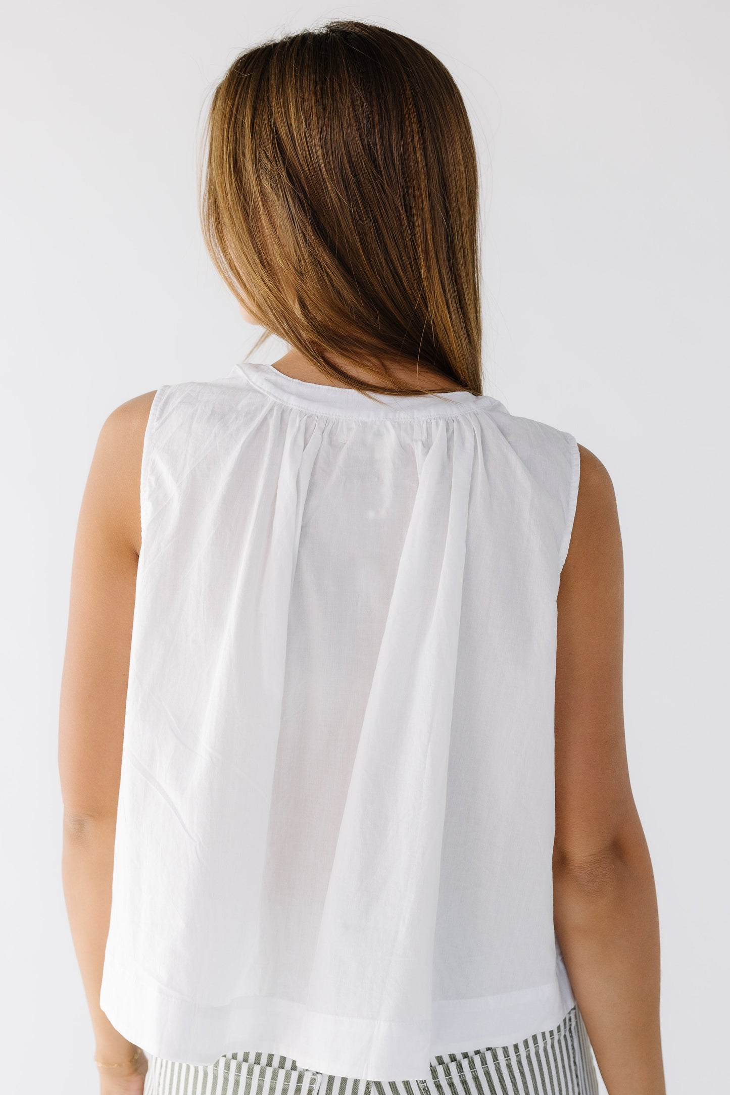Back view of a woman wearing a loose fitting white sleeveless blouse.
