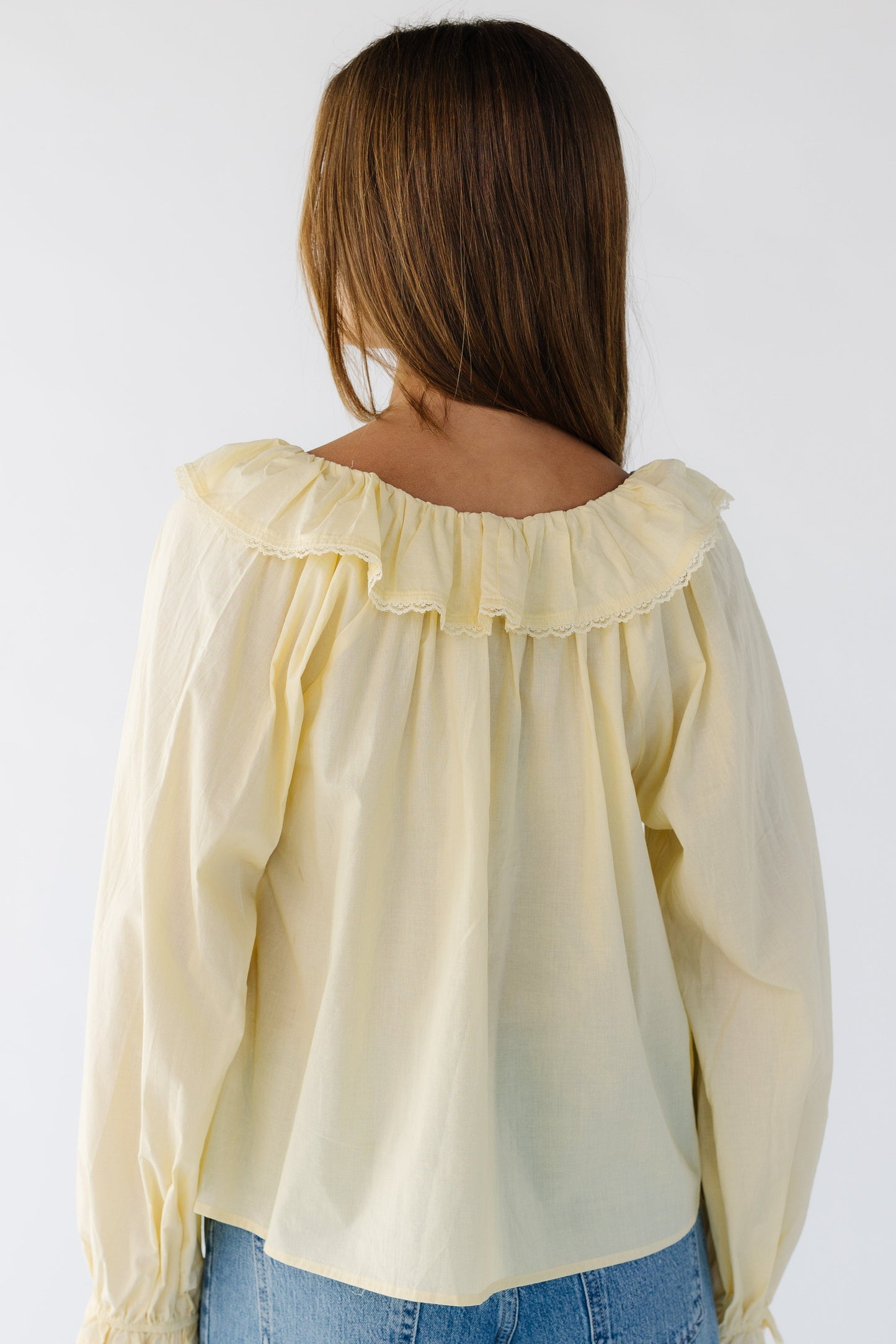 Back view of woman wearing a yellow loose fitting blouse with loose long sleeves and a lace trimmed ruffled collar.