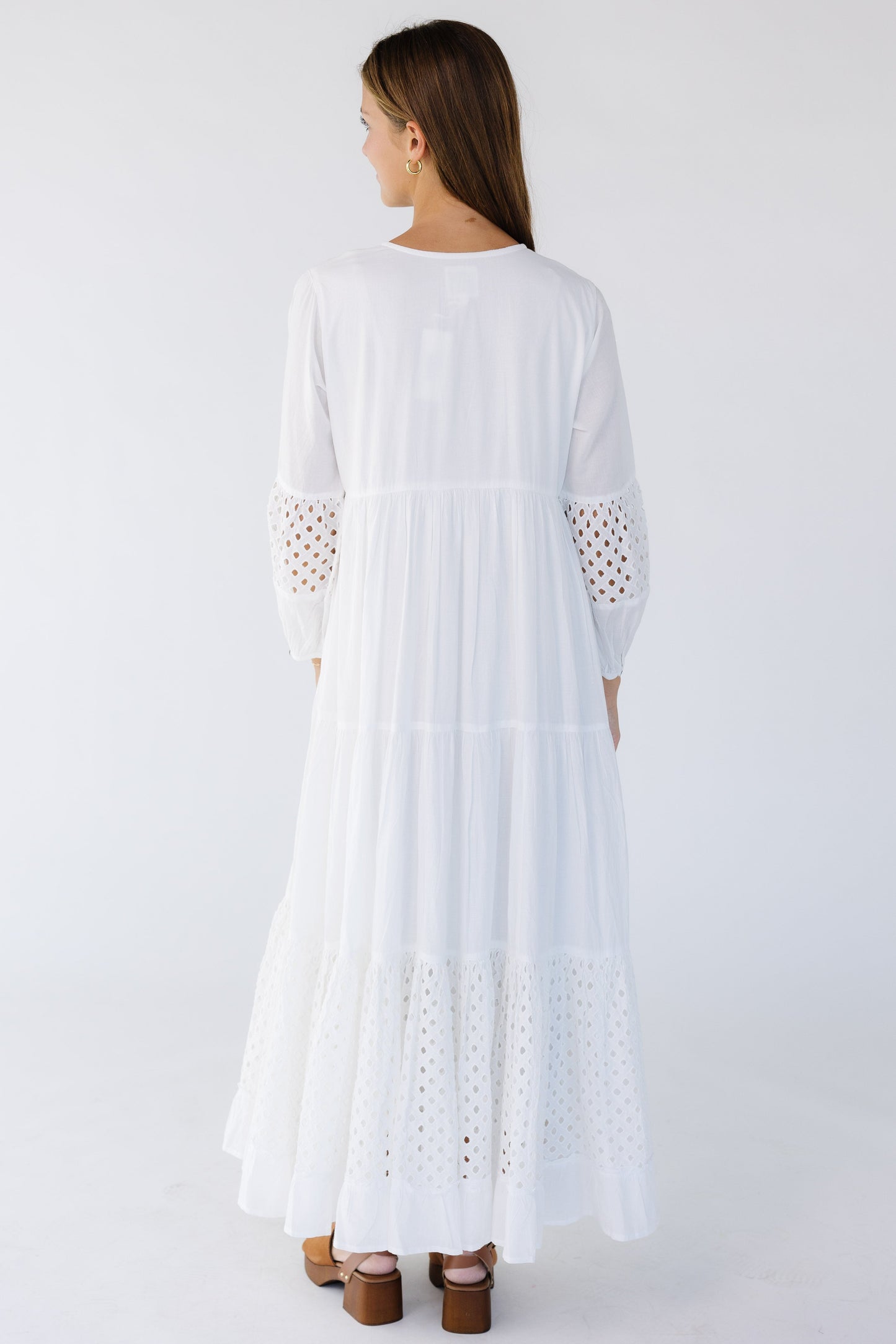 Back view of a woman wearing a white maxi with eyelet tiers and sleeve sections.