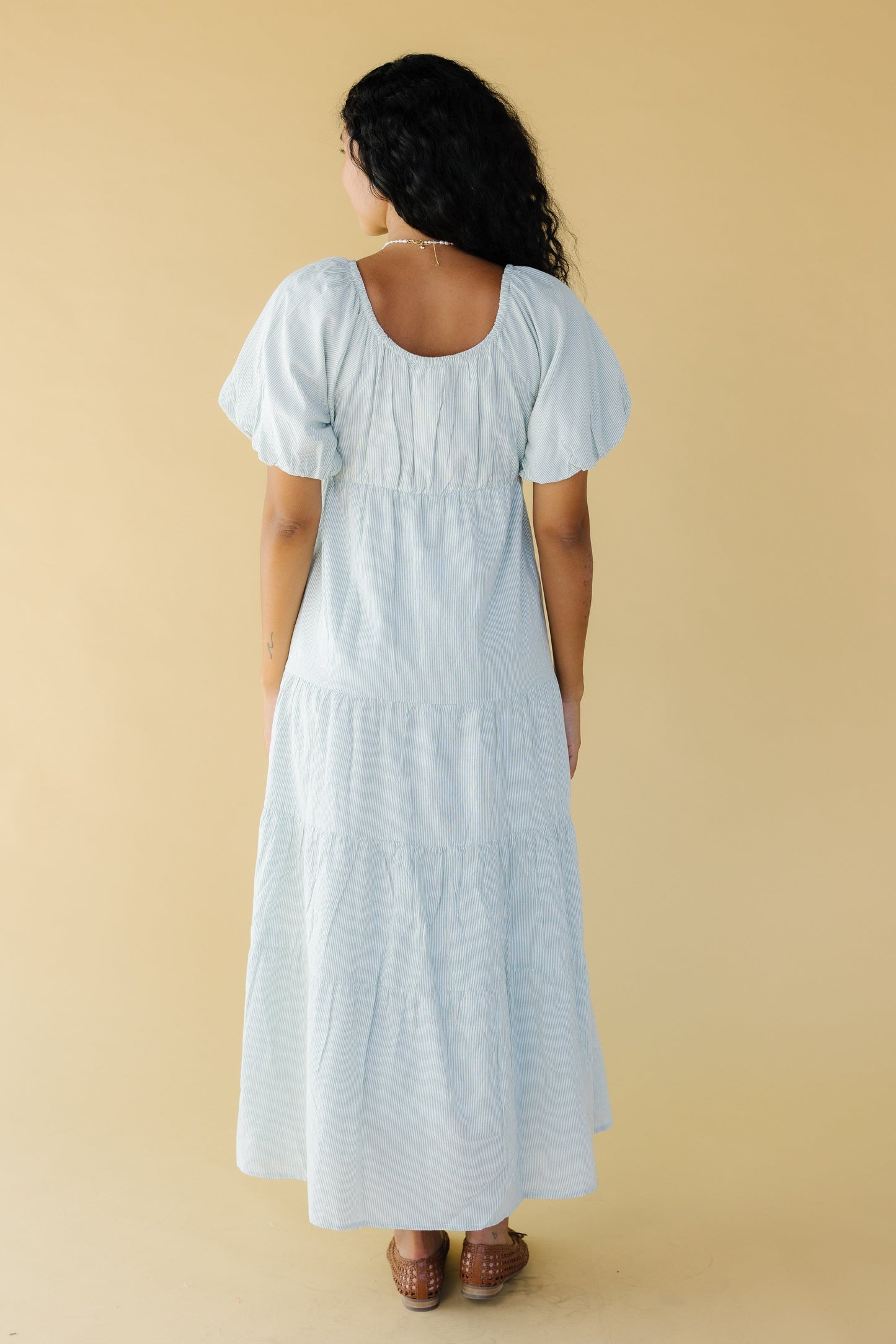 Back view of a woman wearing a green & white stripe midi-maxi dress with balloon sleeves and a scoop neckline.