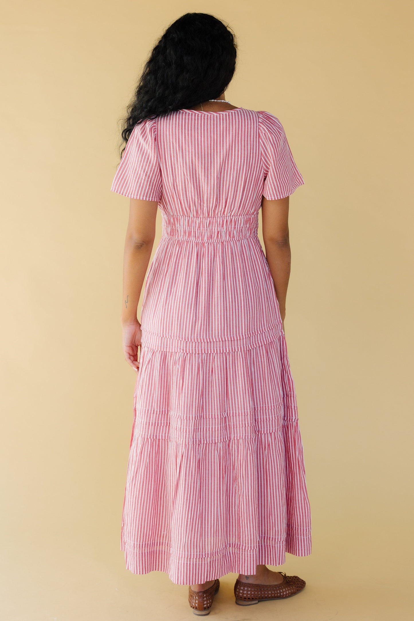 Back view of a young woman wearing a red & white stripe midi-maxi dress with short sleeves and a wide elastic waist.