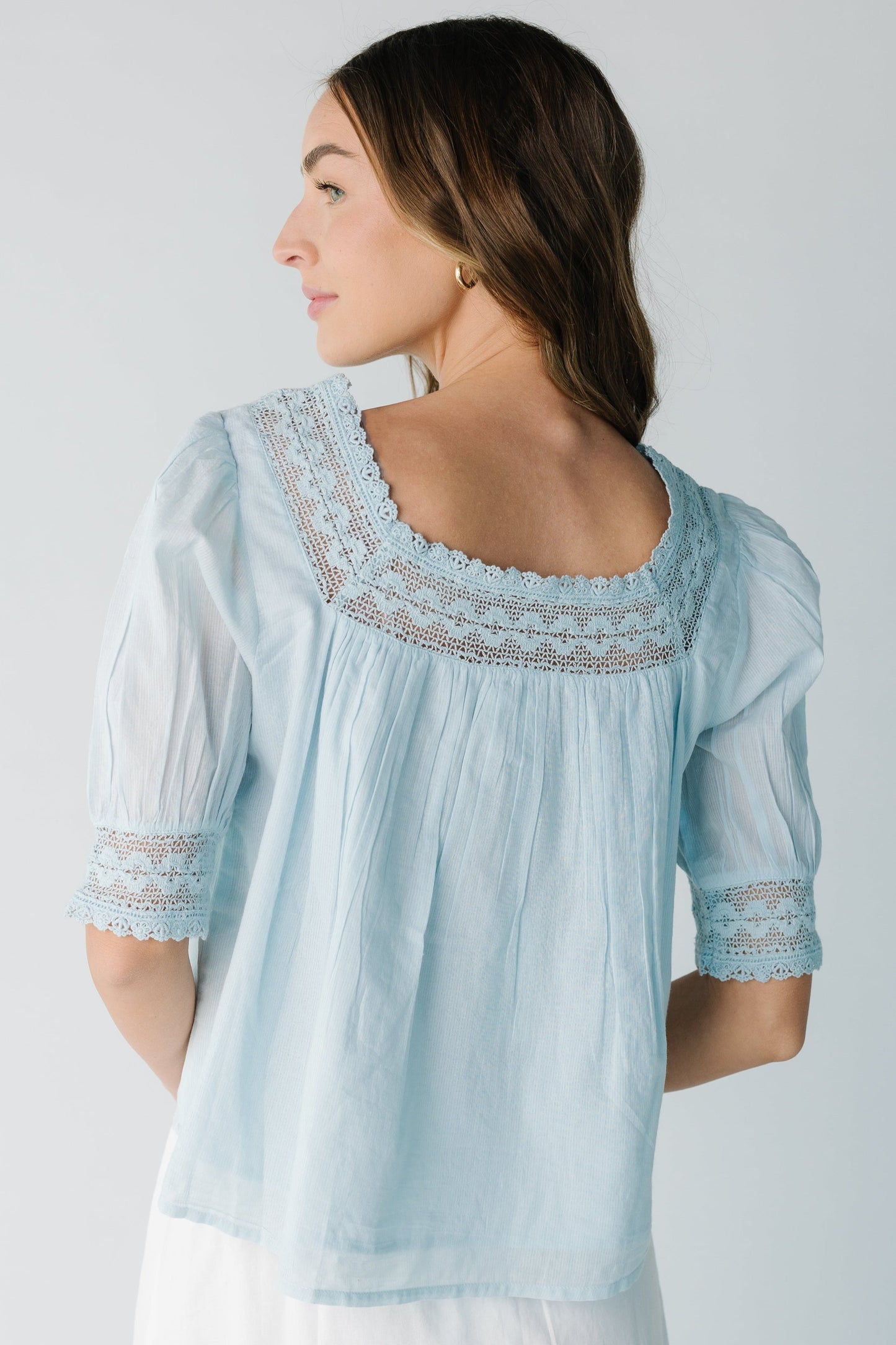 Back view of a woman wearing a light blue blouse with lace neckline