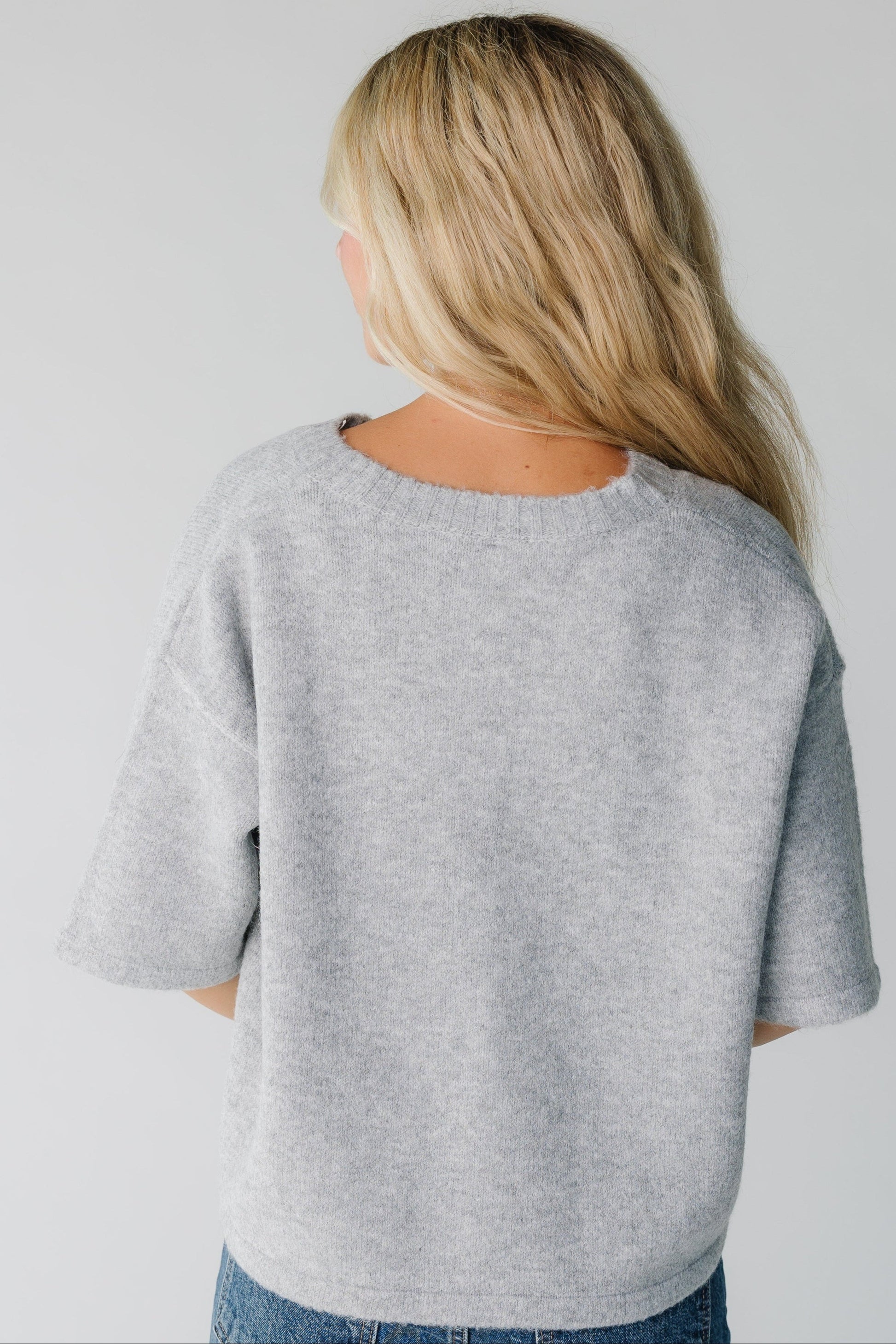 Back view of woman wearing a loose fitting cardigan in grey with half length sleeves