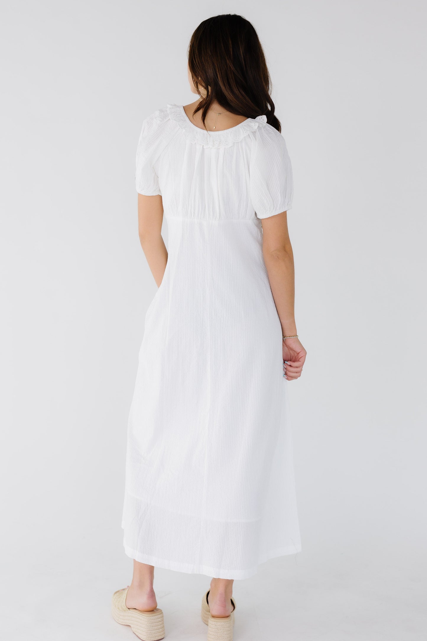 Back view of a woman wearing a white stripe midi dress with an A-line skirt, short puff sleeves and a gathered bodice.