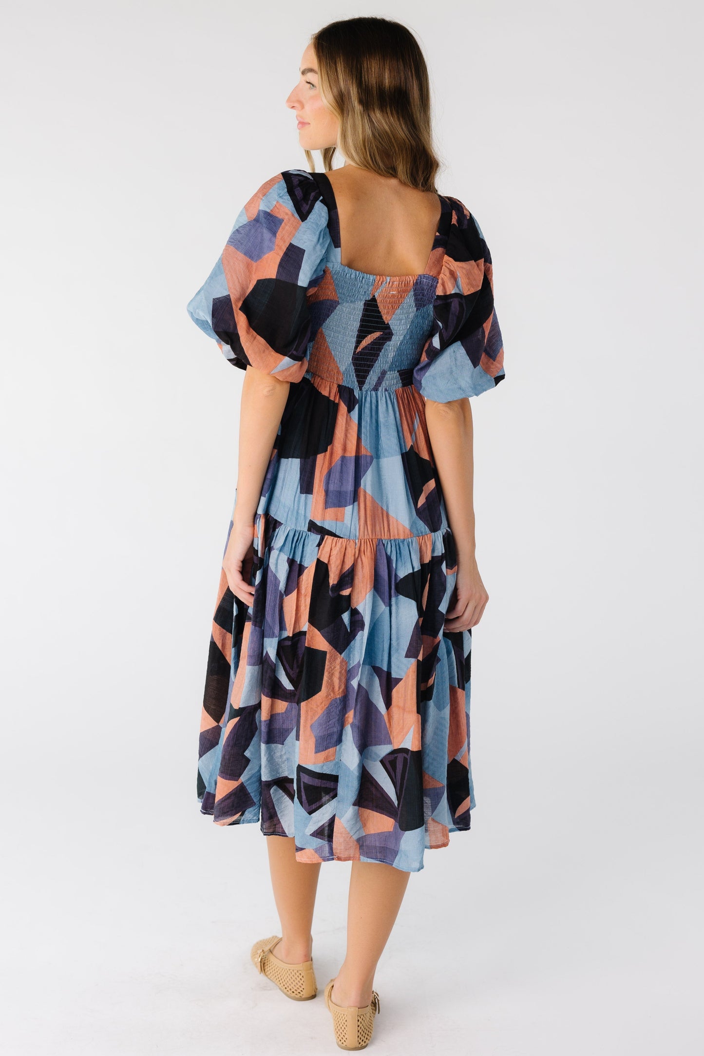 Back view of woman wearing a multi color full dress with elastic smocked back panel and elbow length sleeves