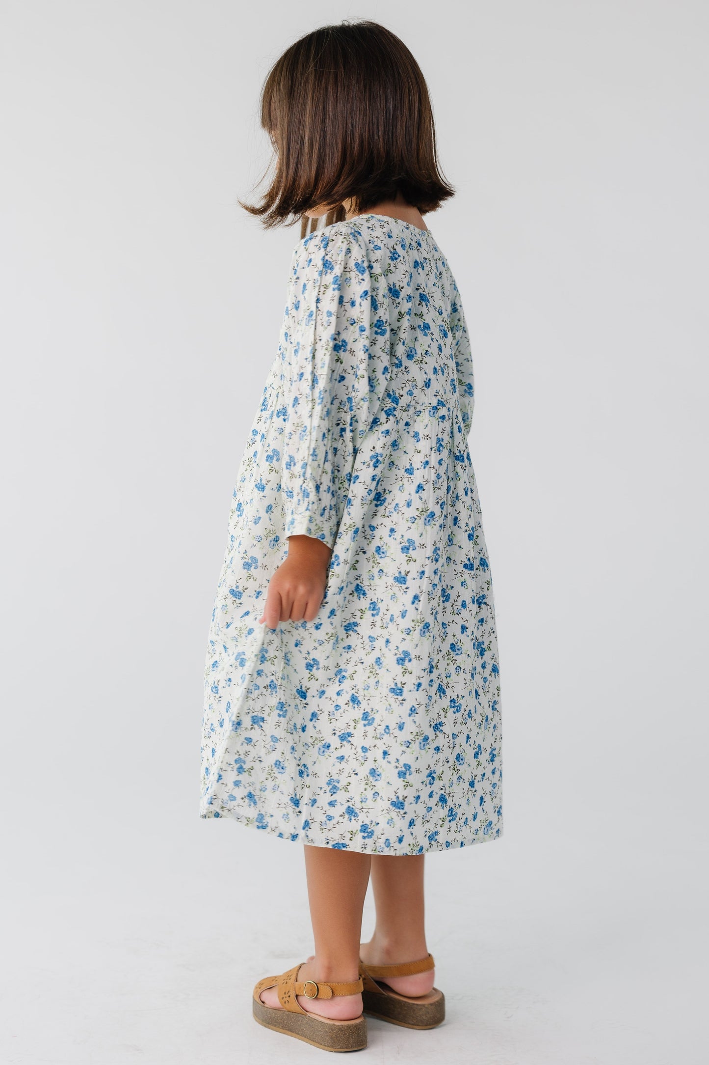 Side view of a girl wearing a long sleeve, loose fitting dress in a white and blue floral print.