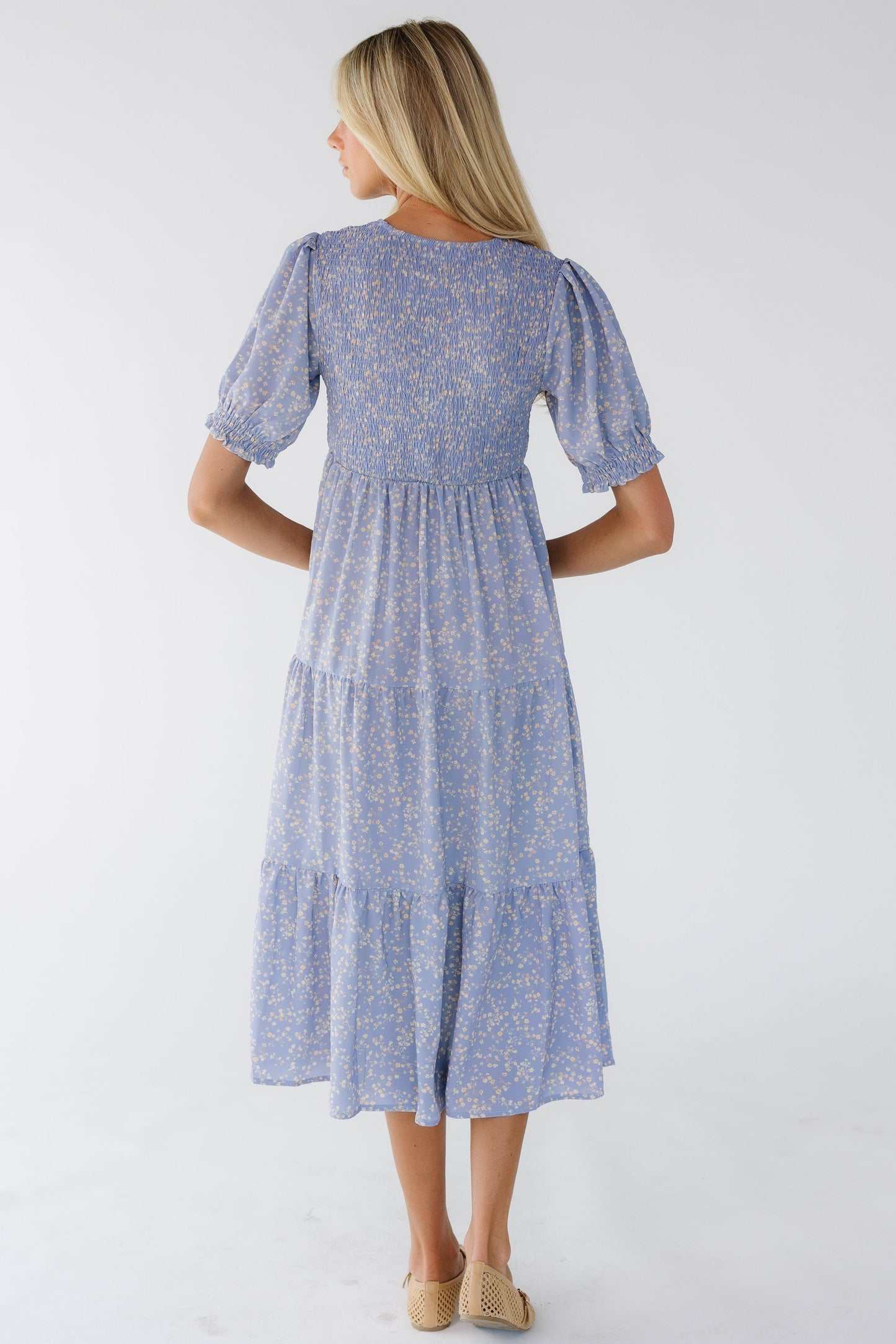 Back view of a woman wearing a light purple floral midi dress with a short sleeves and a smocked bodice.