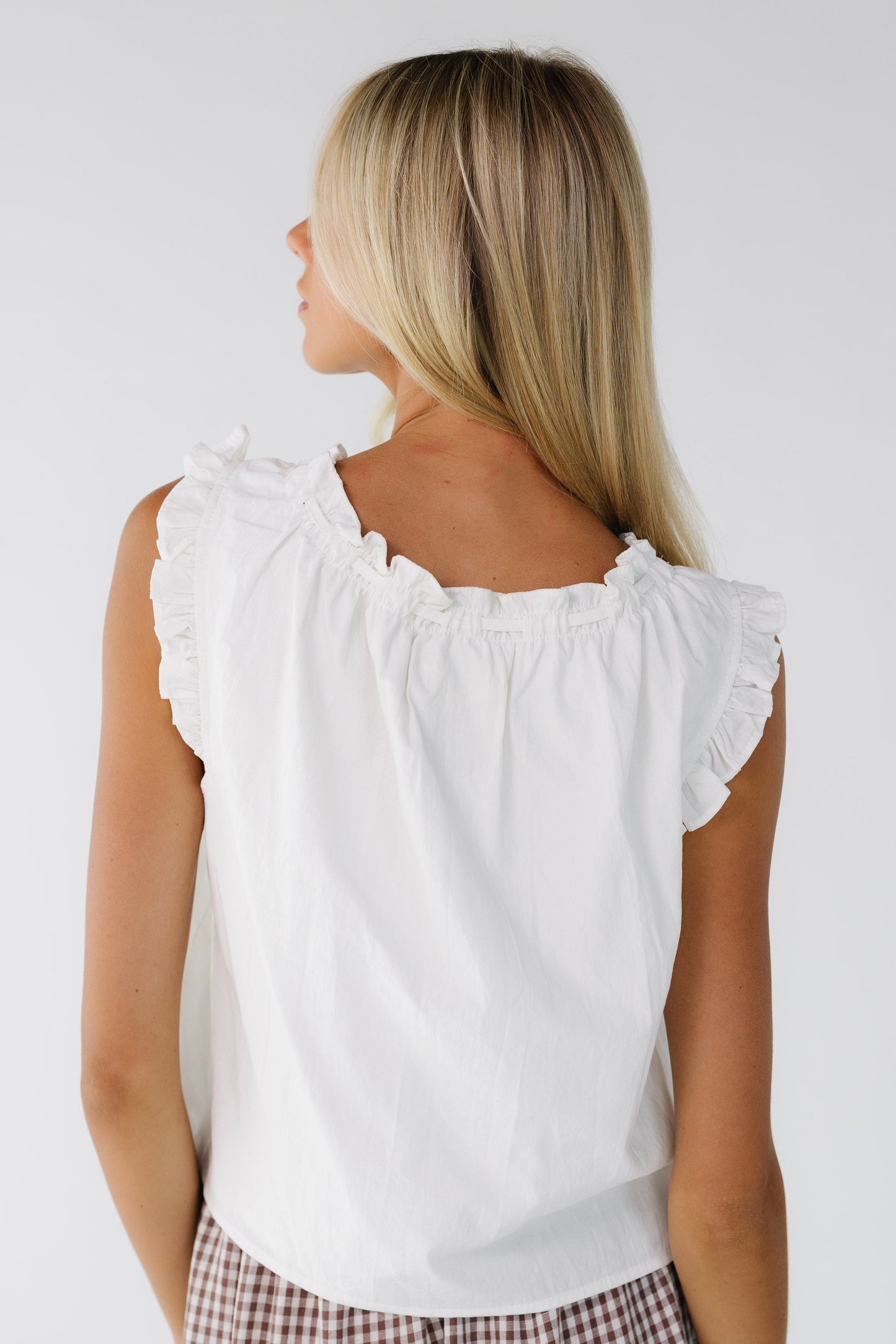 Back view of a young woman wearing a loose fitting white blouse wtih ruffled arm openings and a ruffled neckline.