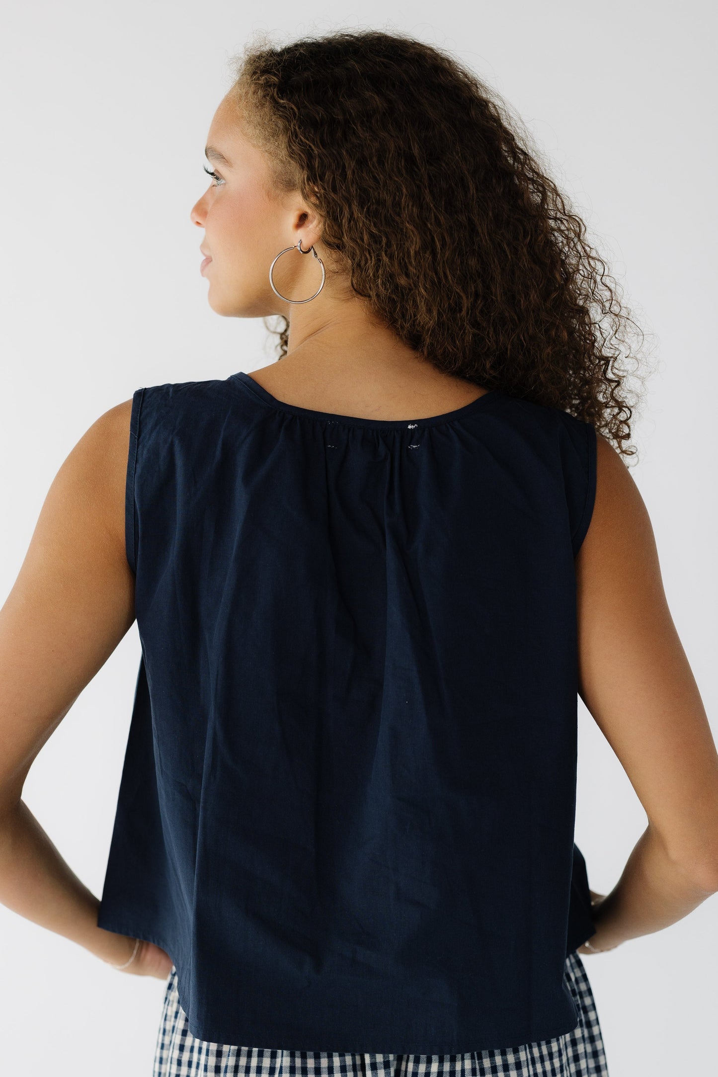 Back view of a teenage girl wearing a navy loose fitting sleeveless blouse.
