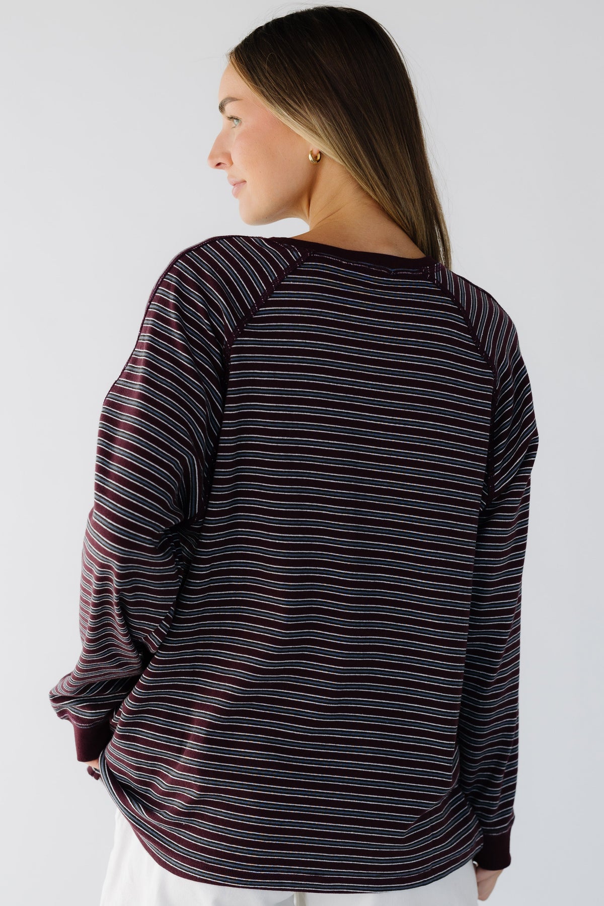 A back view of a woman wearing a burgundy & grey stripe long sleeve tee with exposed seam details.
