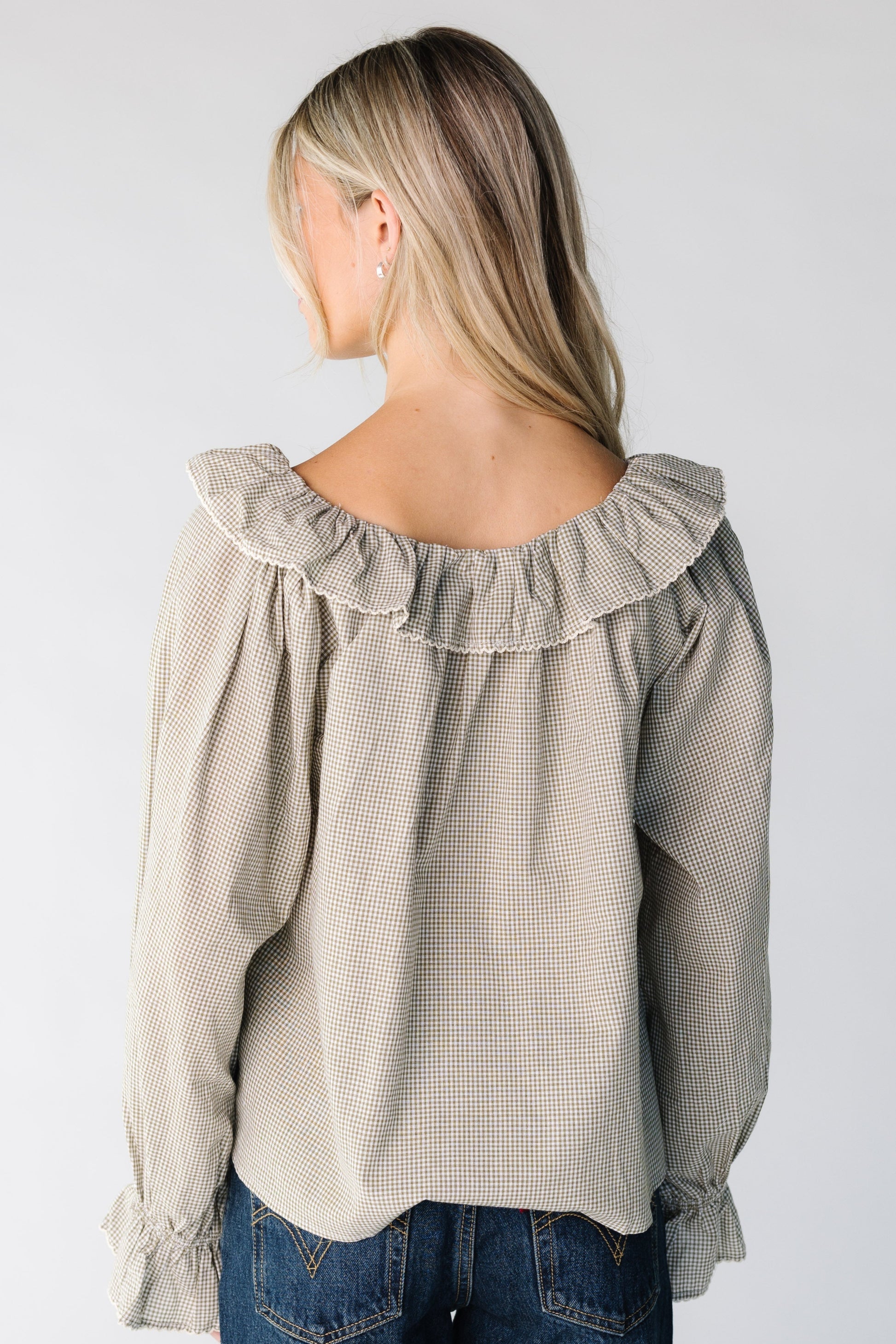 Back view of a woman wearing a sage and   white gingham top with ruffle collar